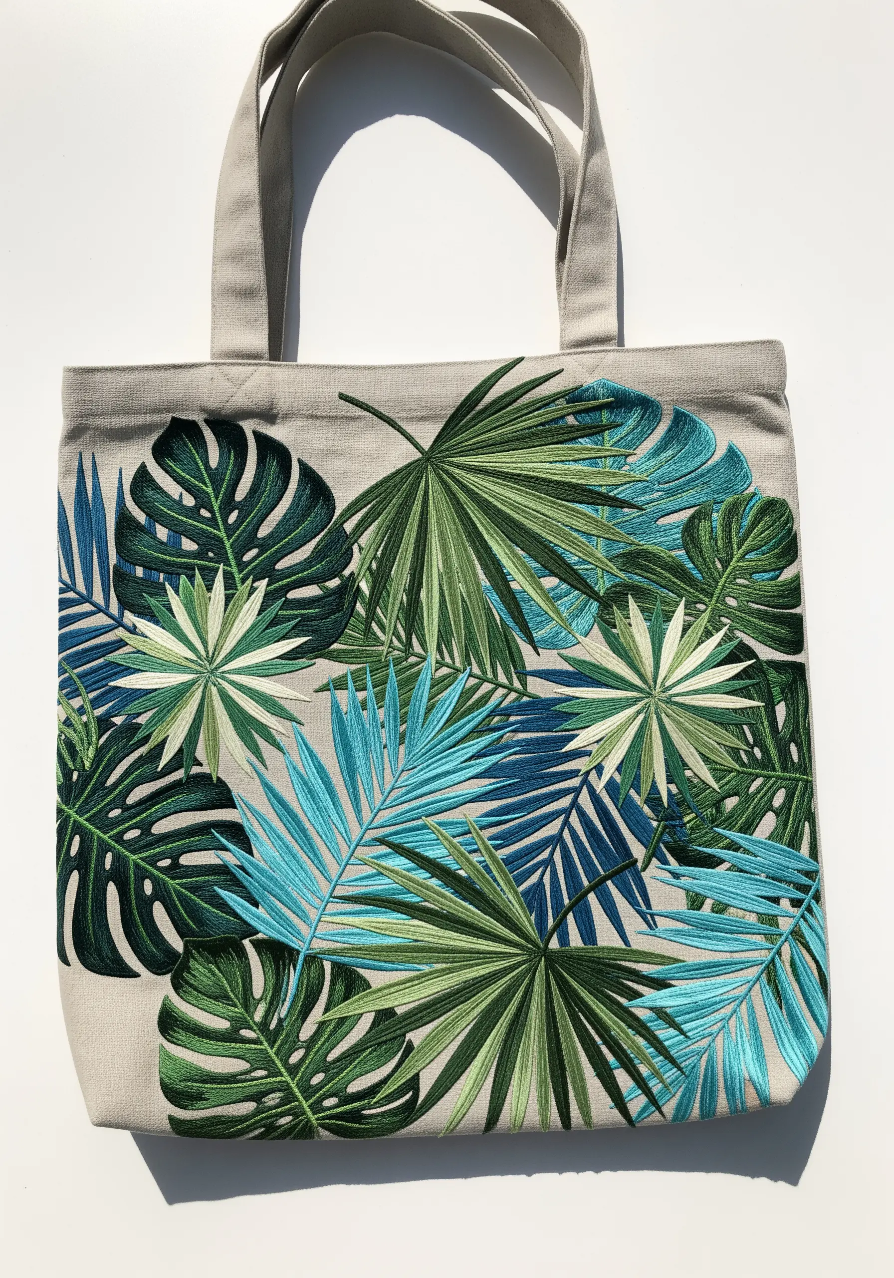 An overlapping collage of tropical leaves in shades of green and blue on a canvas tote.