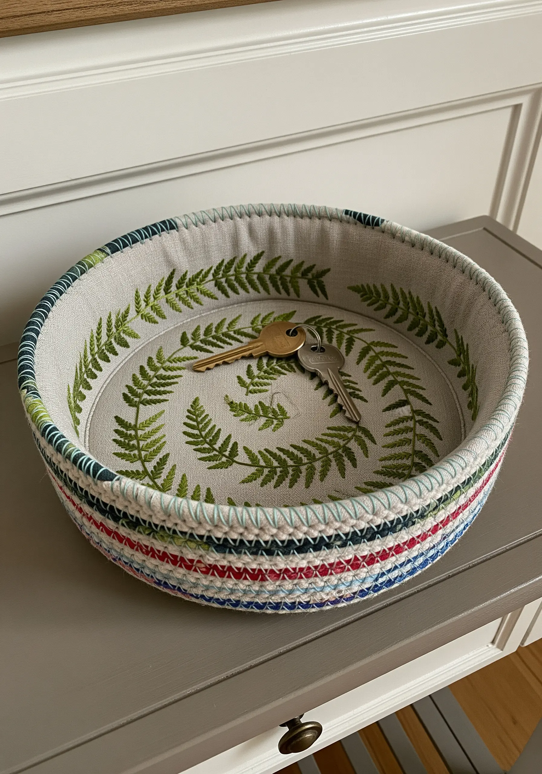 A coiled rope bowl with a wreath of green embroidered ferns on the inside base.