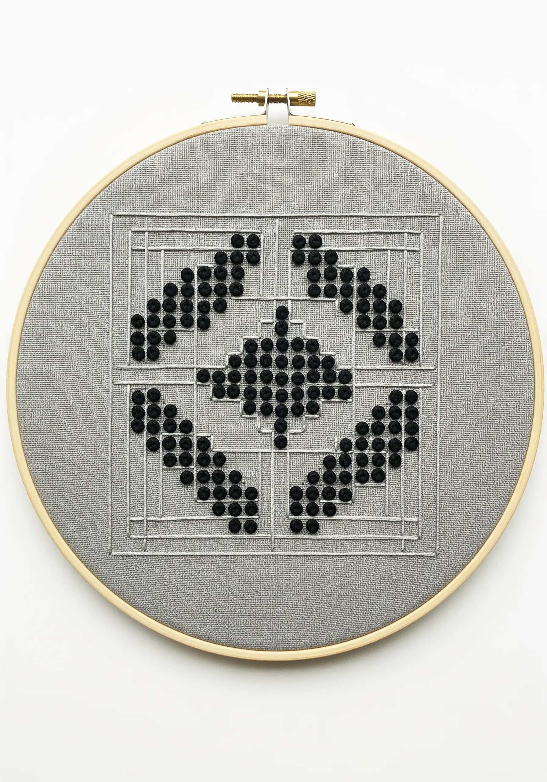 A geometric pattern on gray fabric using black French knots within a silver backstitch grid.