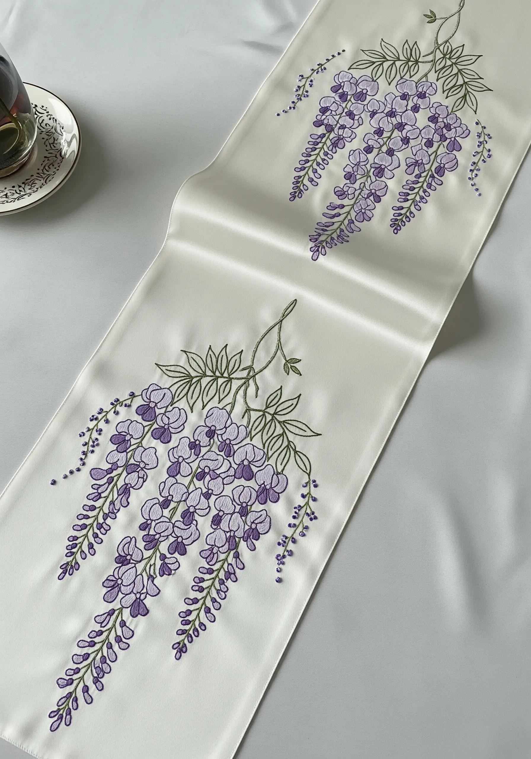 Purple wisteria embroidery with layered French knots on a white satin table runner.