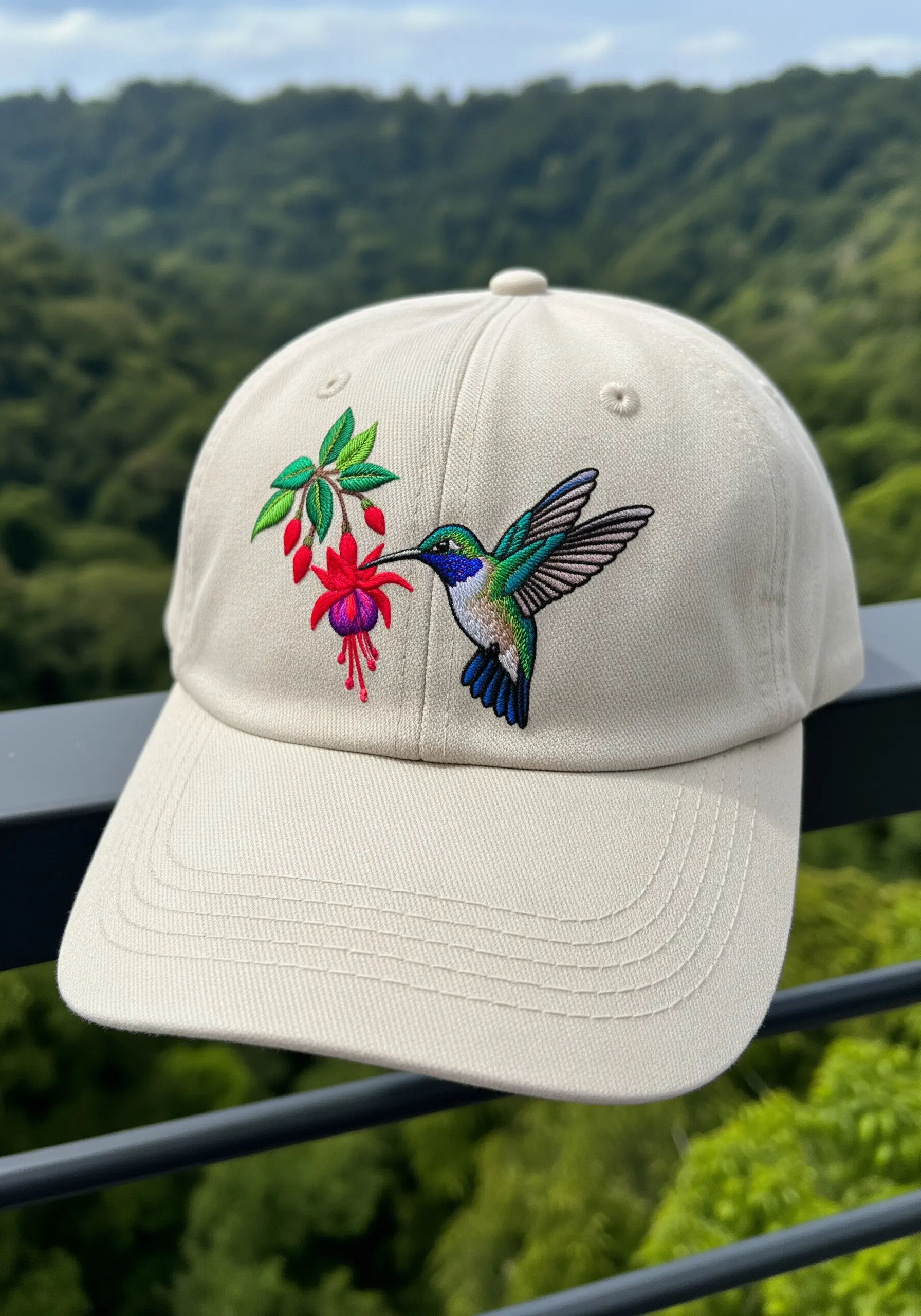 A detailed embroidered hummingbird with iridescent feathers feeding from a pink fuchsia flower on a cap.