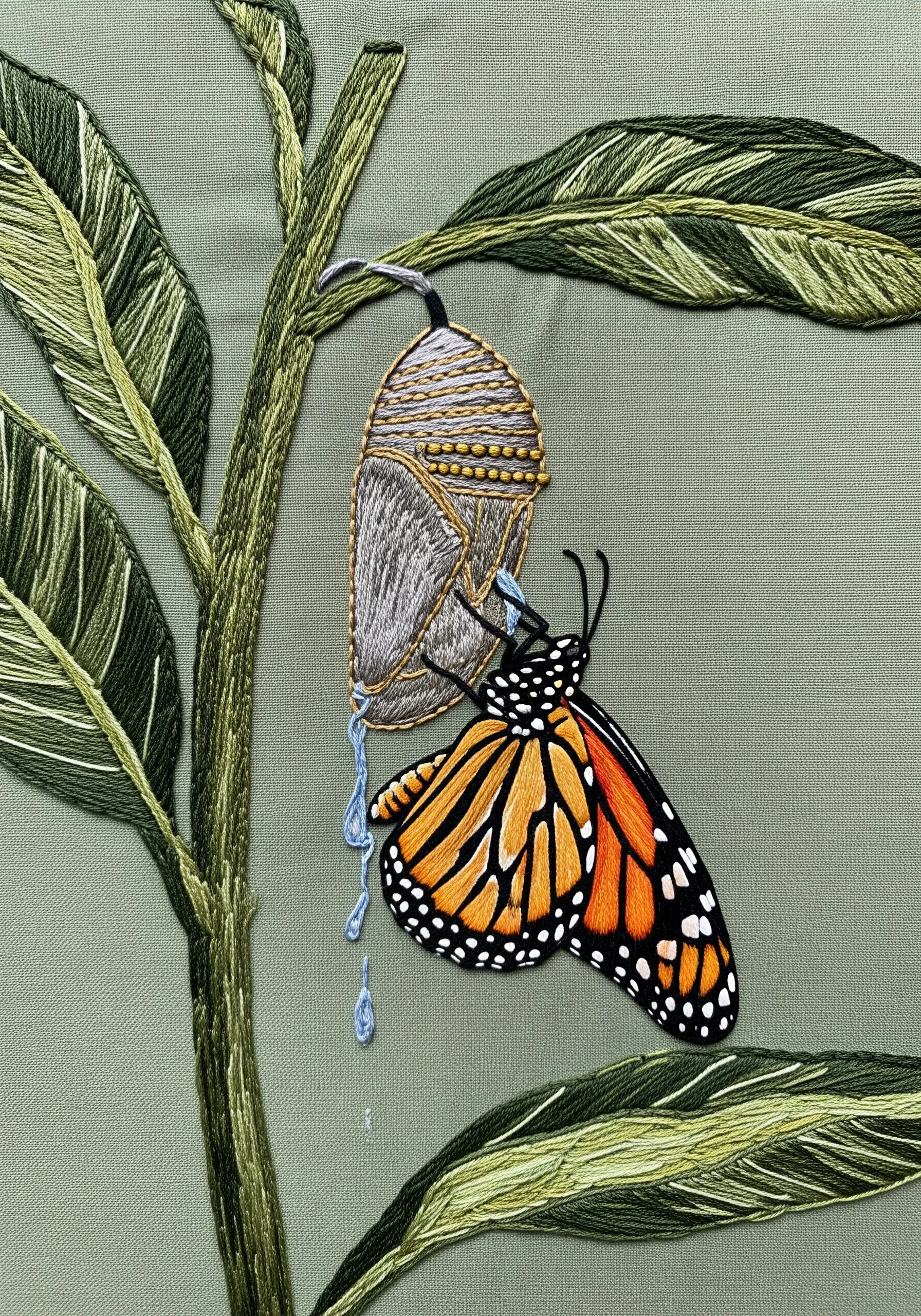 A monarch butterfly emerging from its chrysalis, with detailed leaves and stitched water drips.