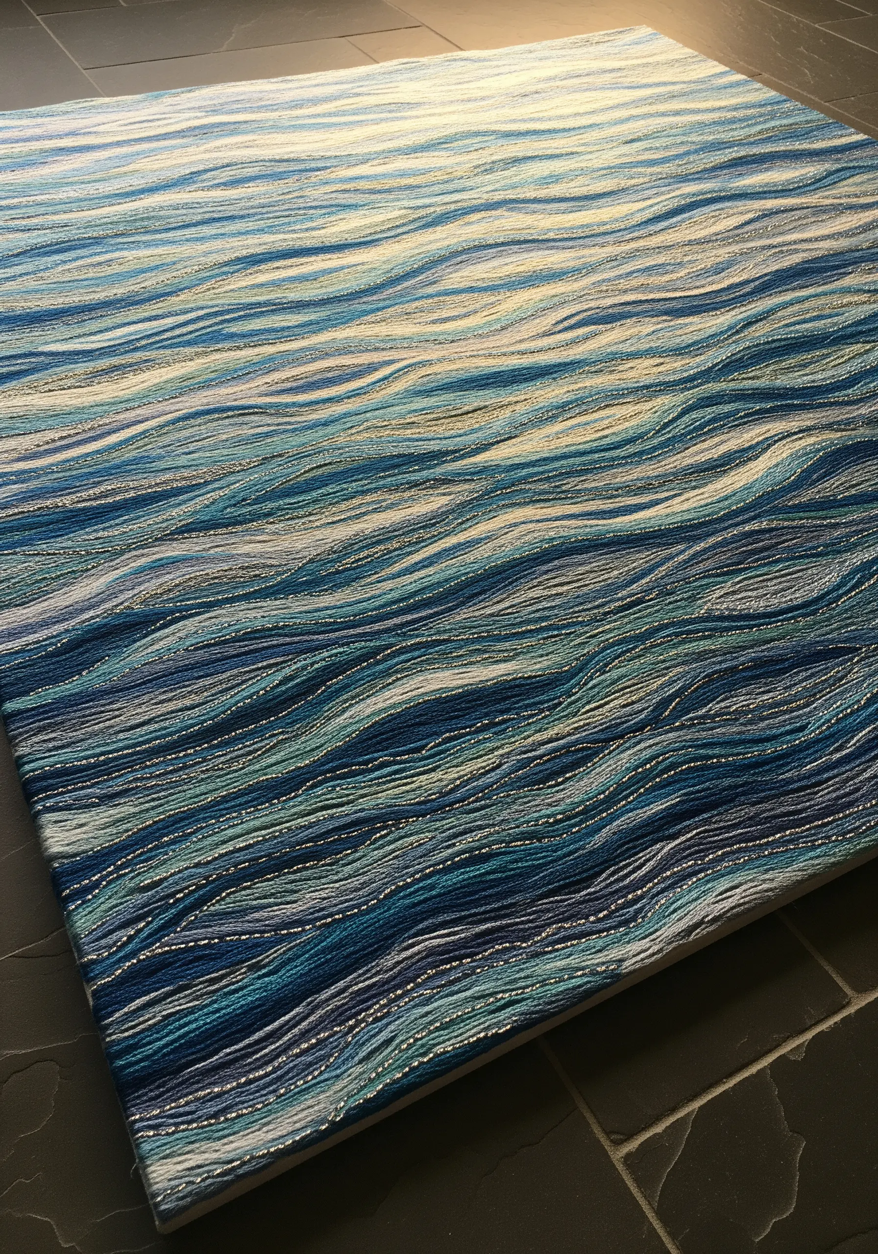 A large canvas filled with horizontal lines of embroidery in shades of blue, creating a water texture.