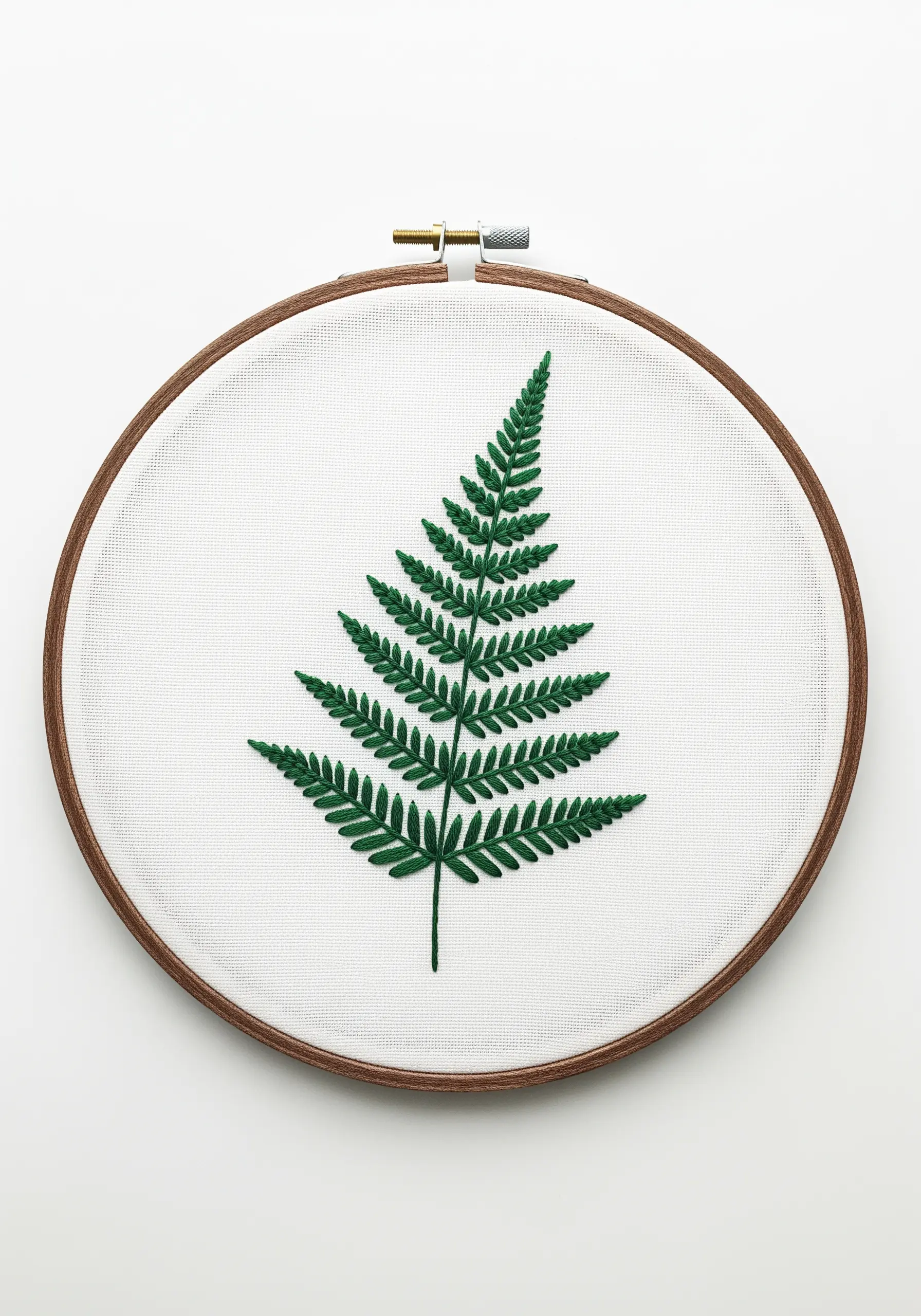 A single, detailed fern frond embroidered in dark green on white Aida cloth.