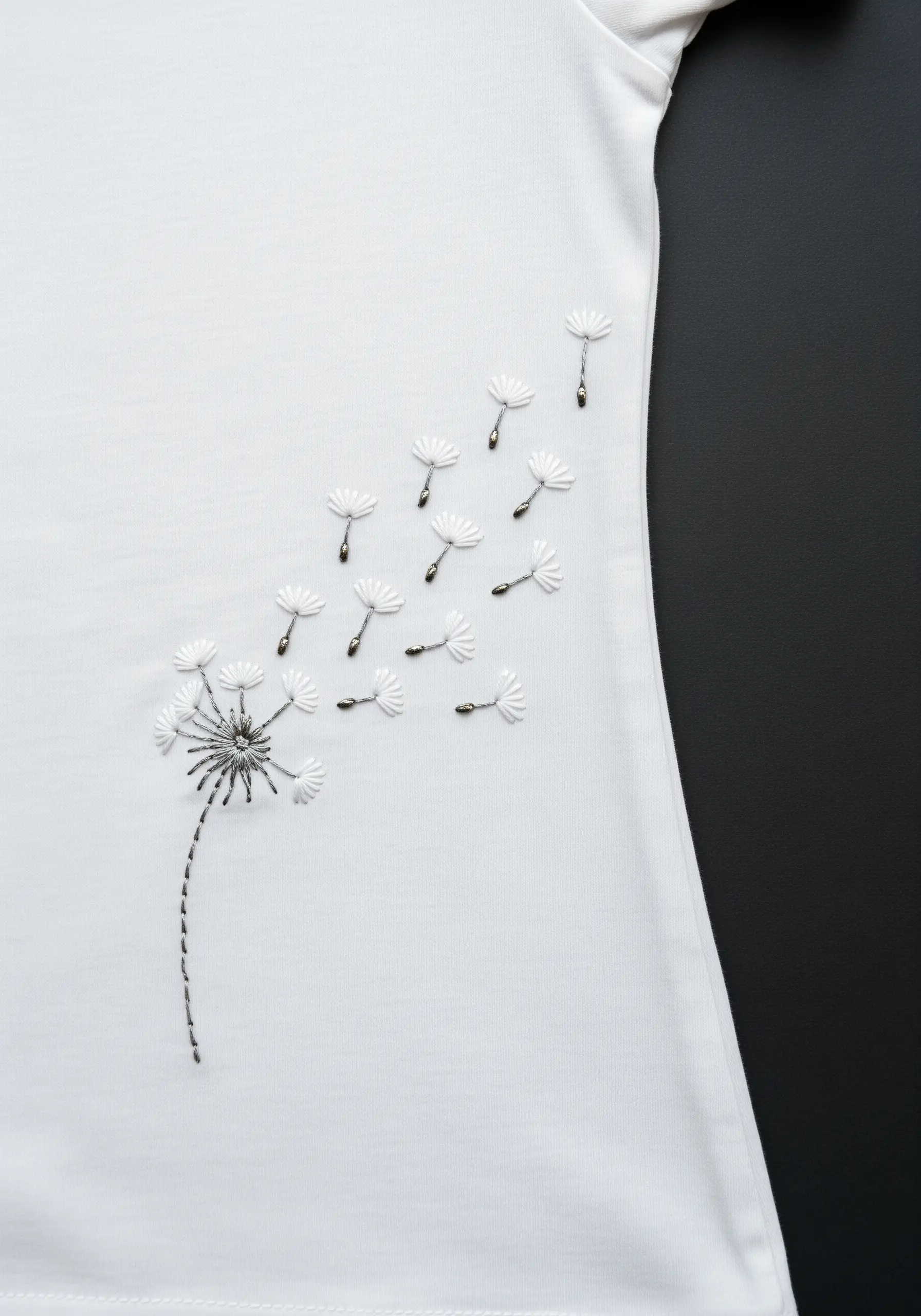 Dandelion with seeds blowing away, embroidered in silver and white thread.
