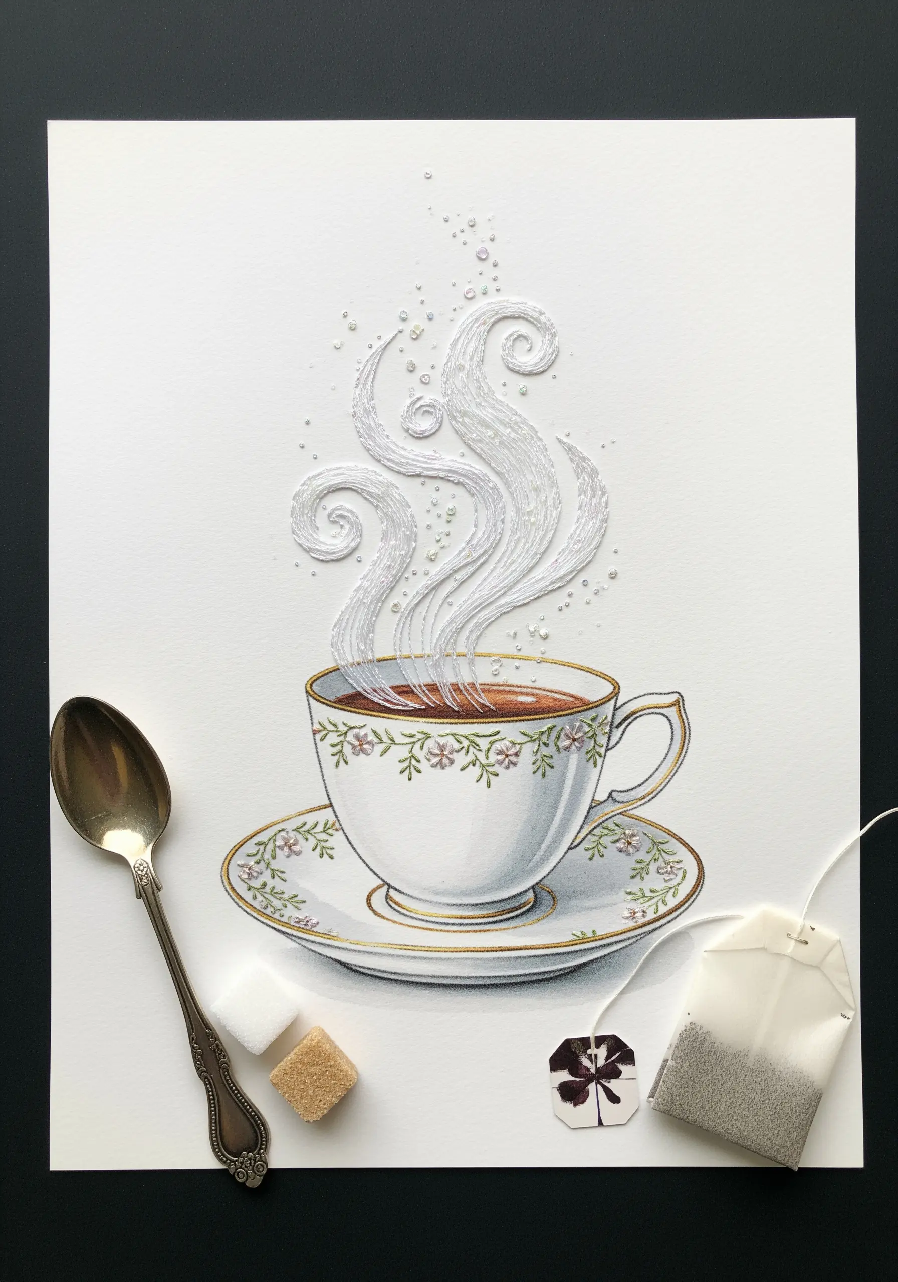 An illustrated teacup with delicate white thread embroidered as swirling steam, accented with beads.