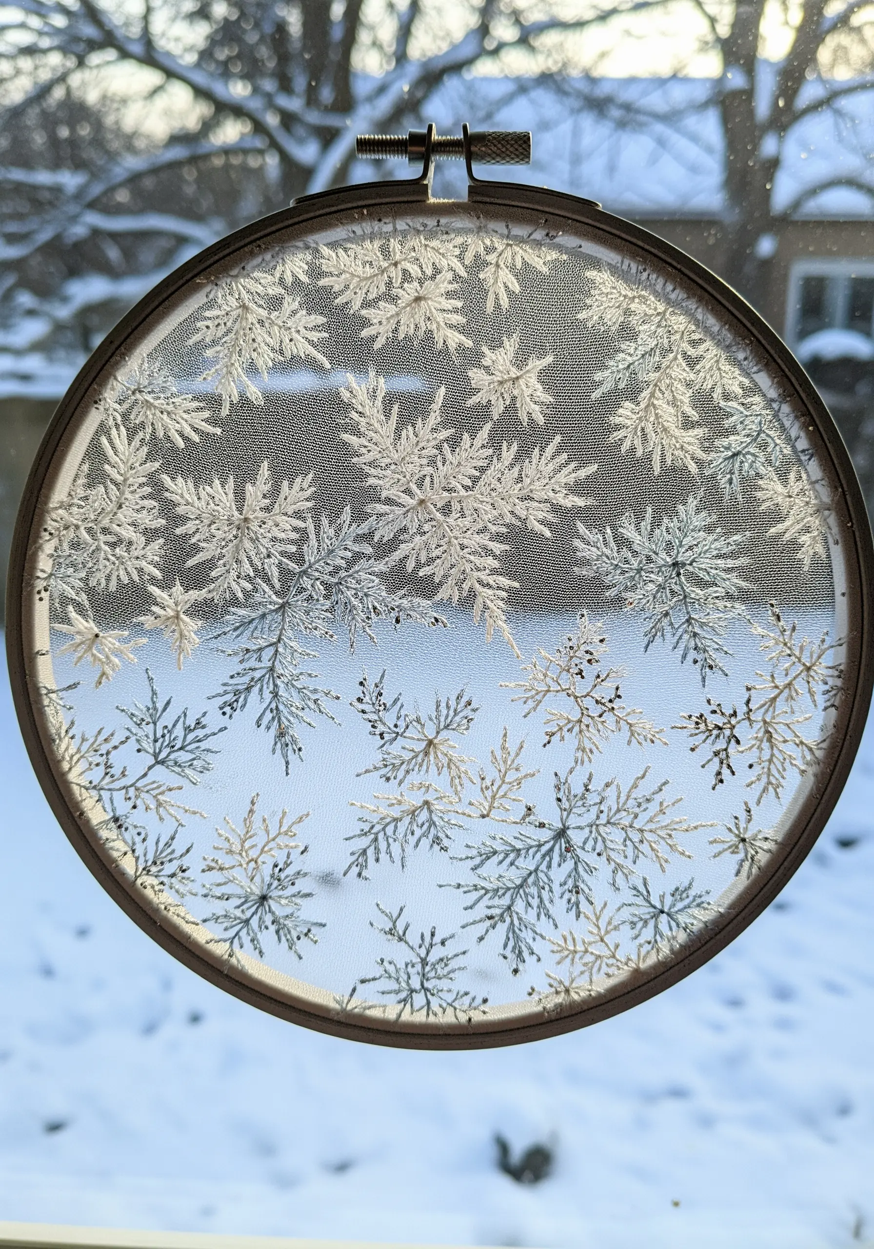 Frost-like fern stitches in white and silver embroidered on sheer tulle inside a hoop.