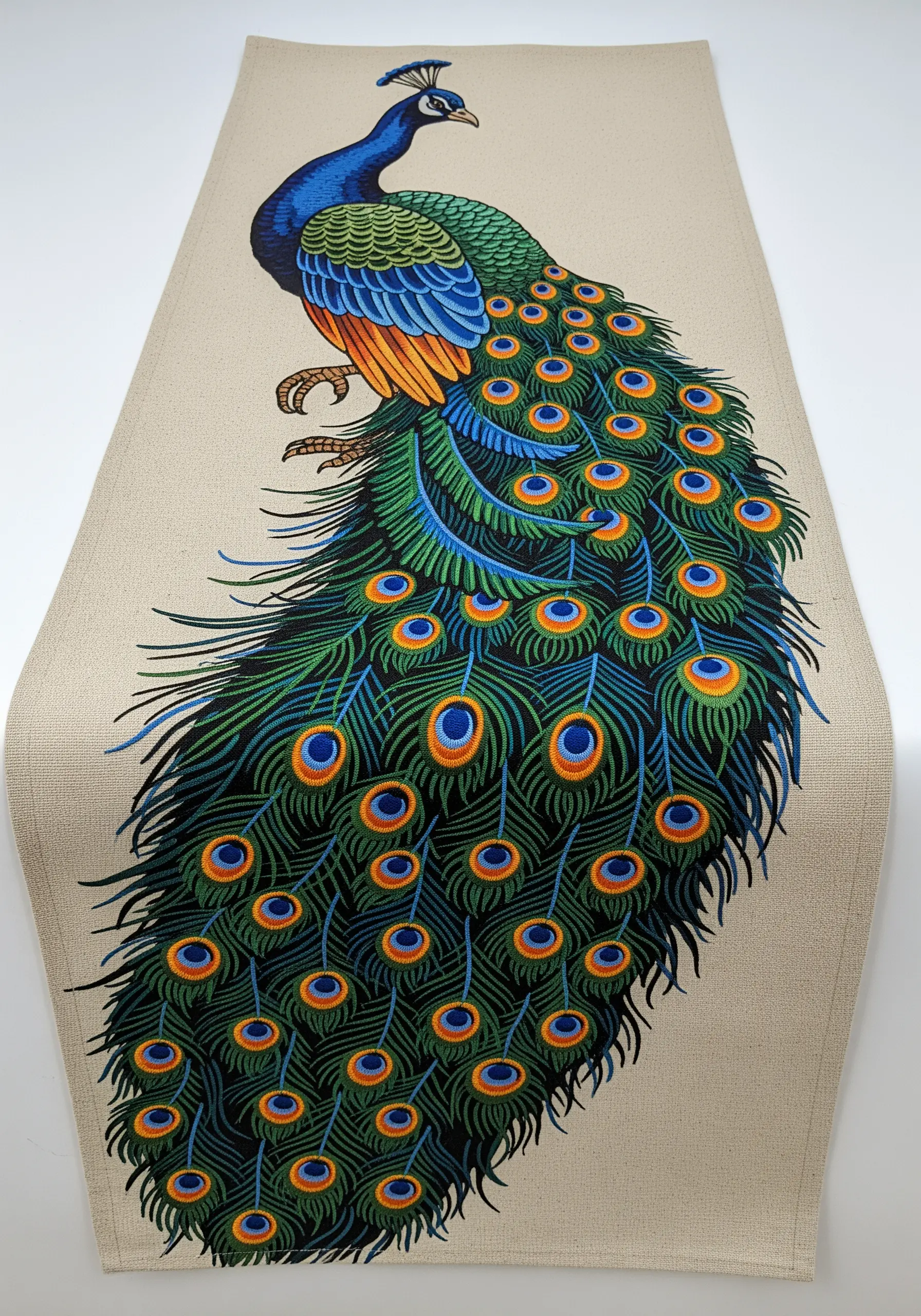 A large embroidered peacock with a long, flowing tail on a neutral table runner.