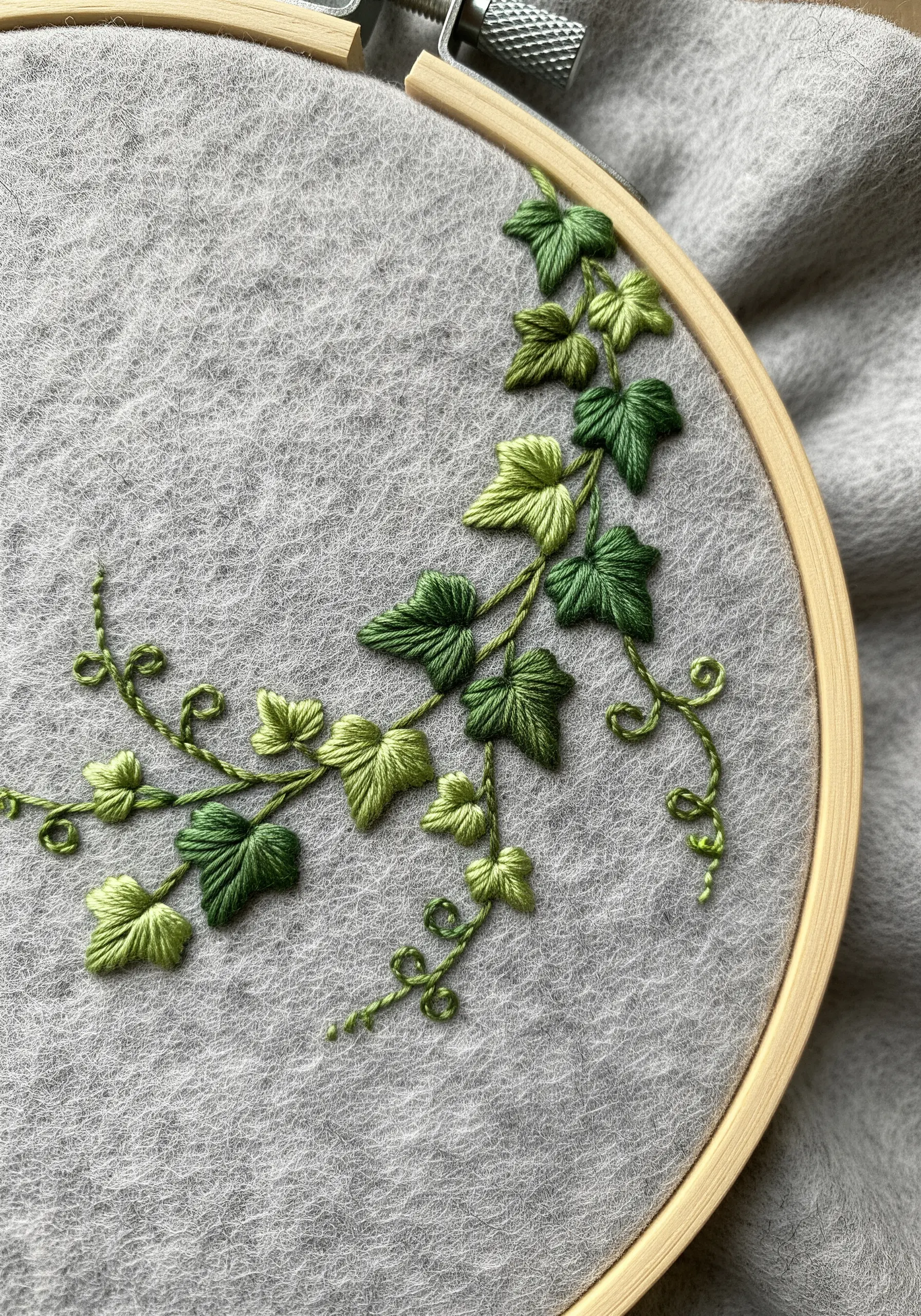 Embroidered ivy vine with variegated green leaves on a gray felt fabric.