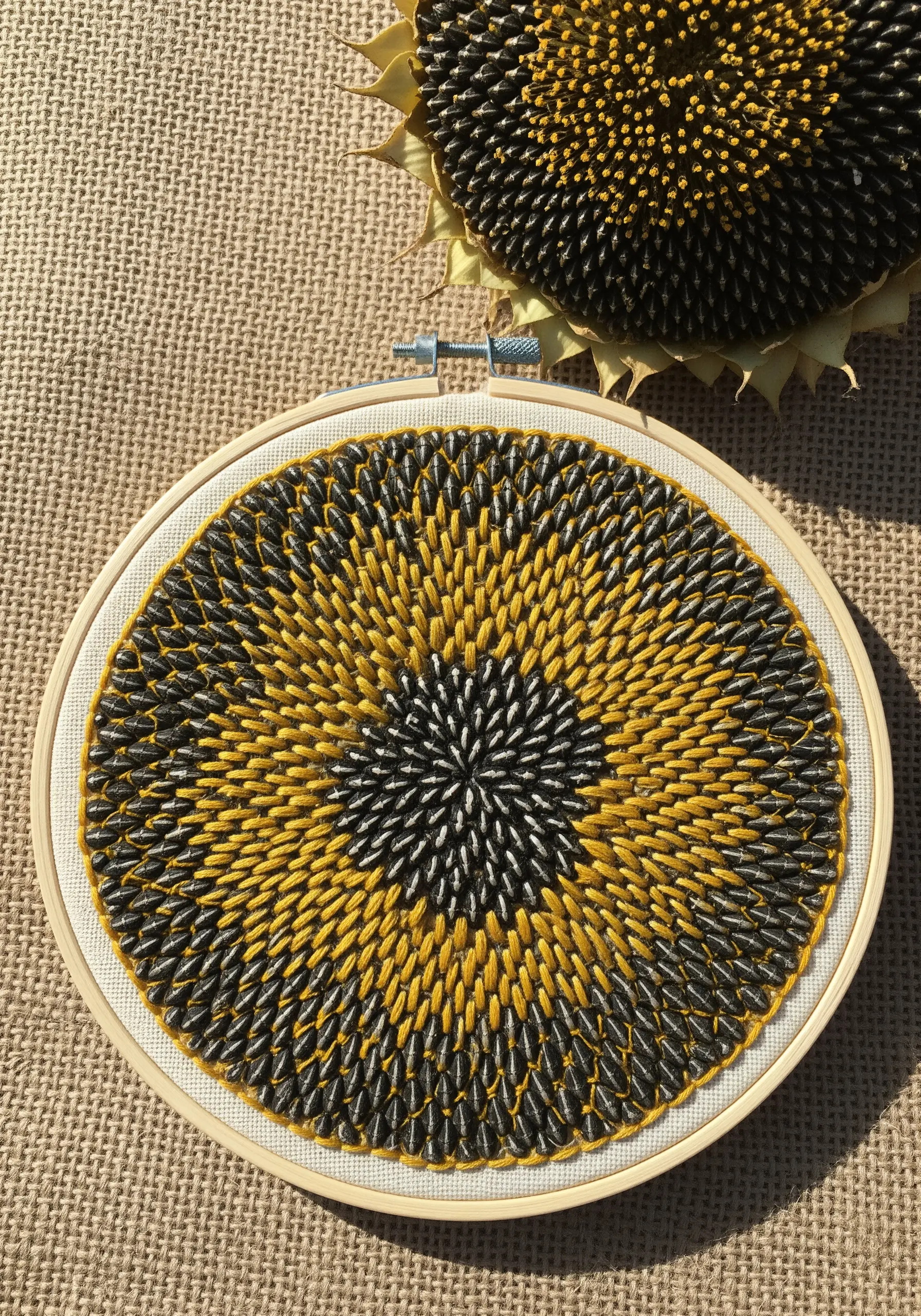 The center of a sunflower recreated with precisely angled straight stitches in yellow and black.