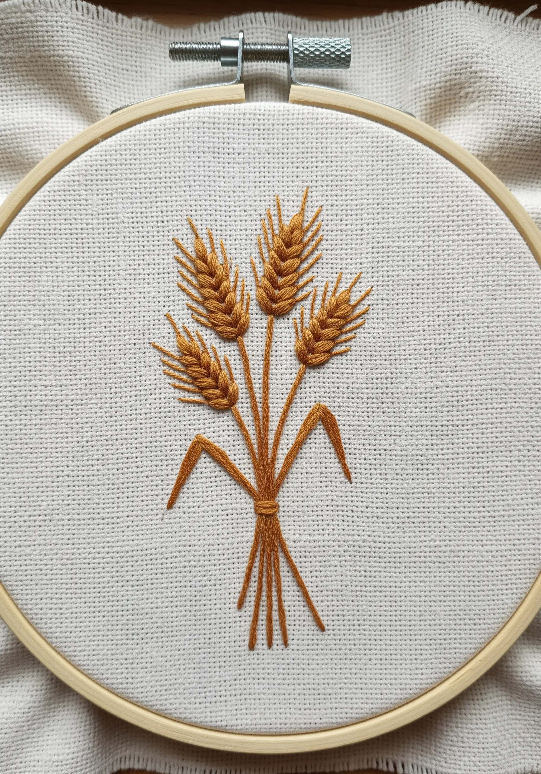 A tied sheaf of wheat embroidered on white fabric using fly stitch and stem stitch.