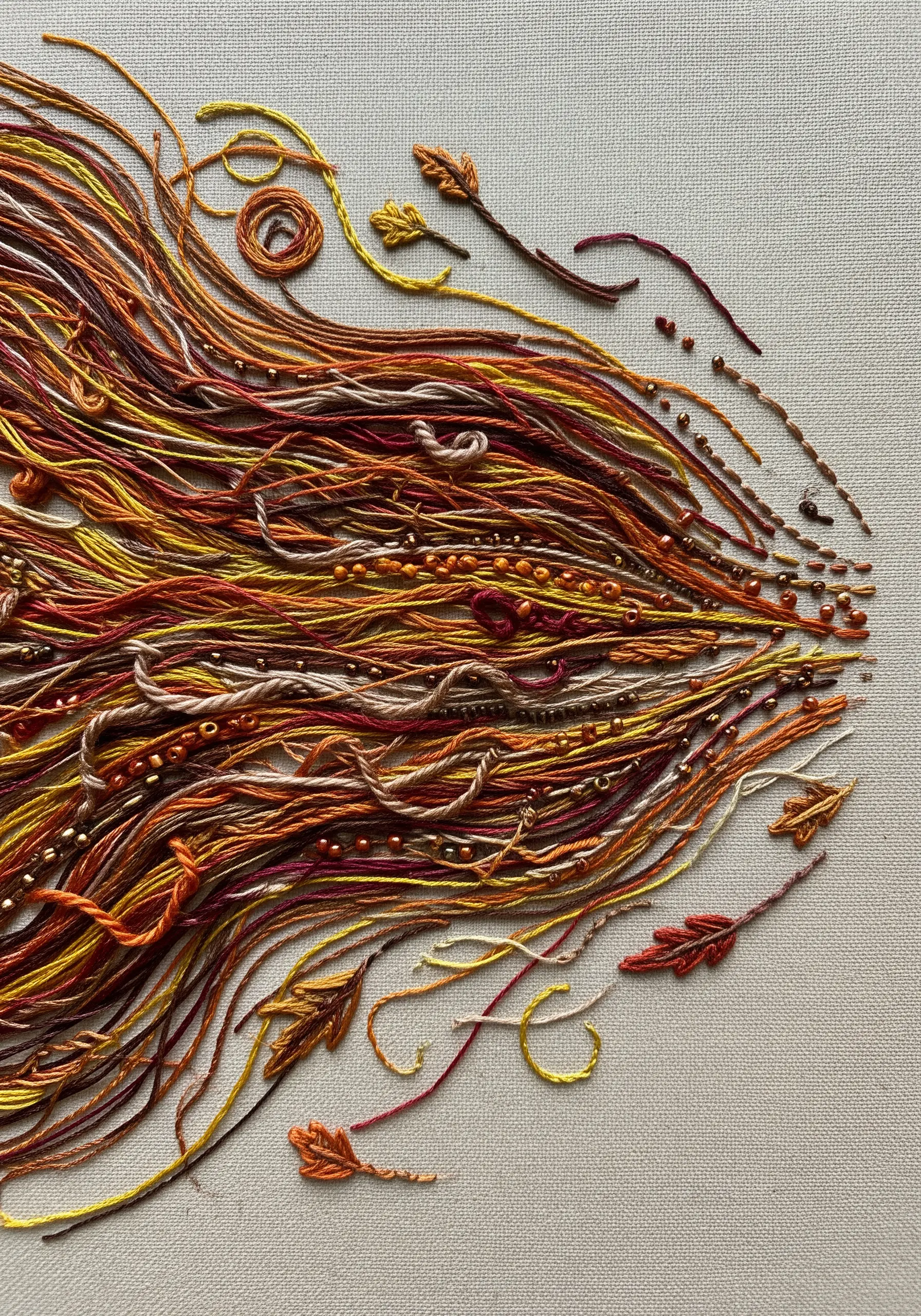 Abstract embroidery of autumn wind using loose threads, beads, and tiny leaf stitches.