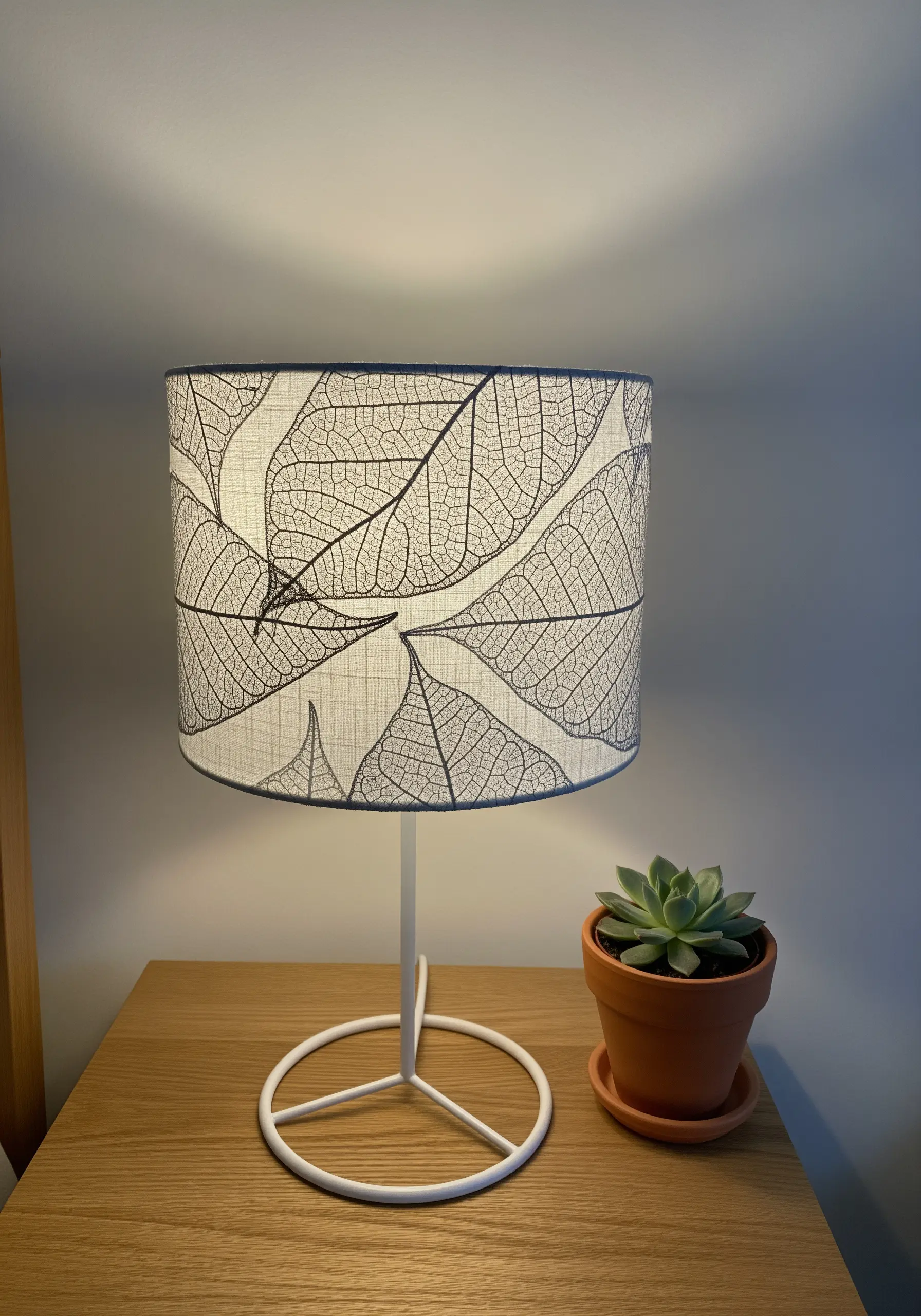 Lampshade decorated with delicate black-thread embroidery of leaf skeletons.