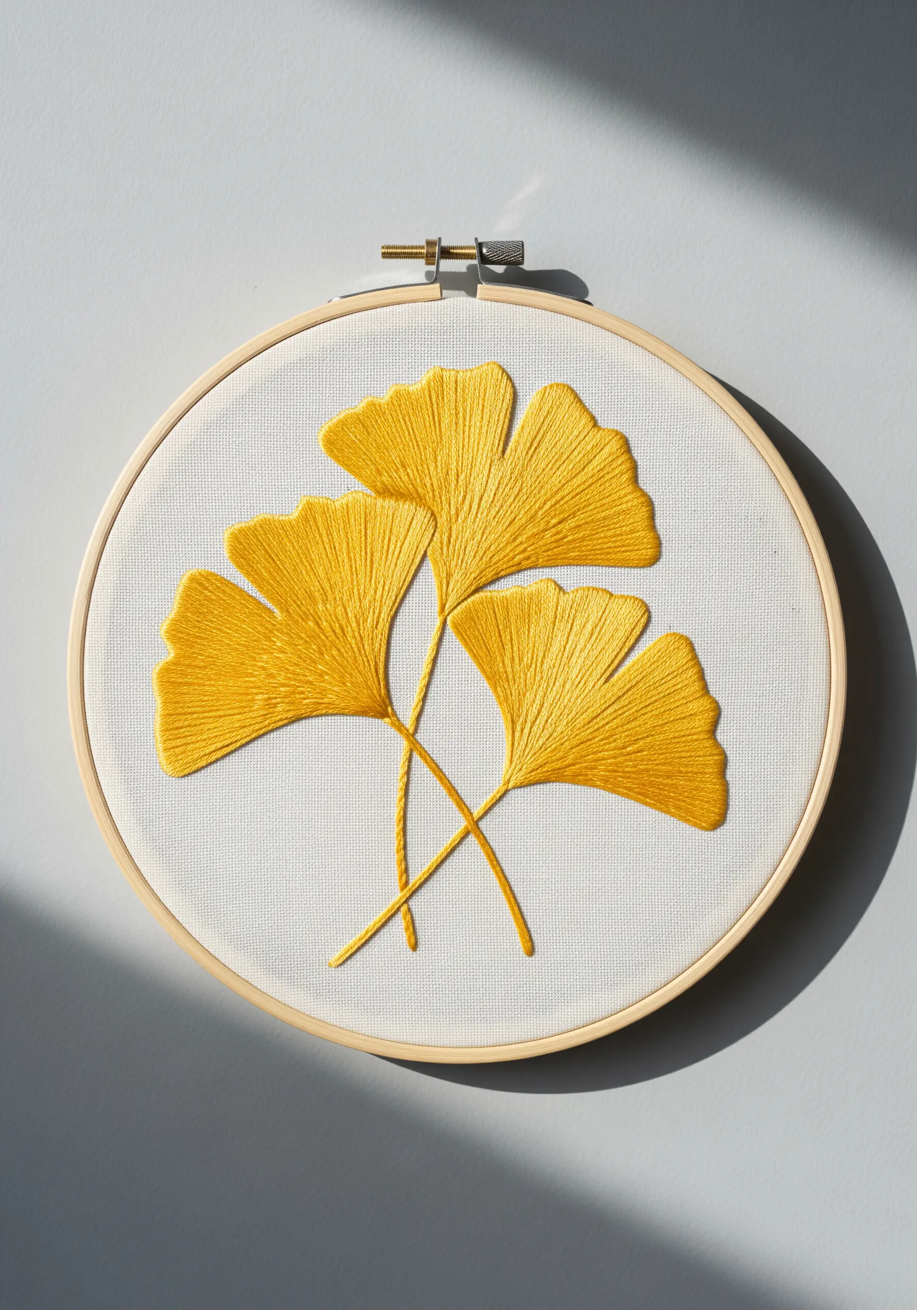 Three golden ginkgo leaves embroidered with directional satin stitch on white fabric.