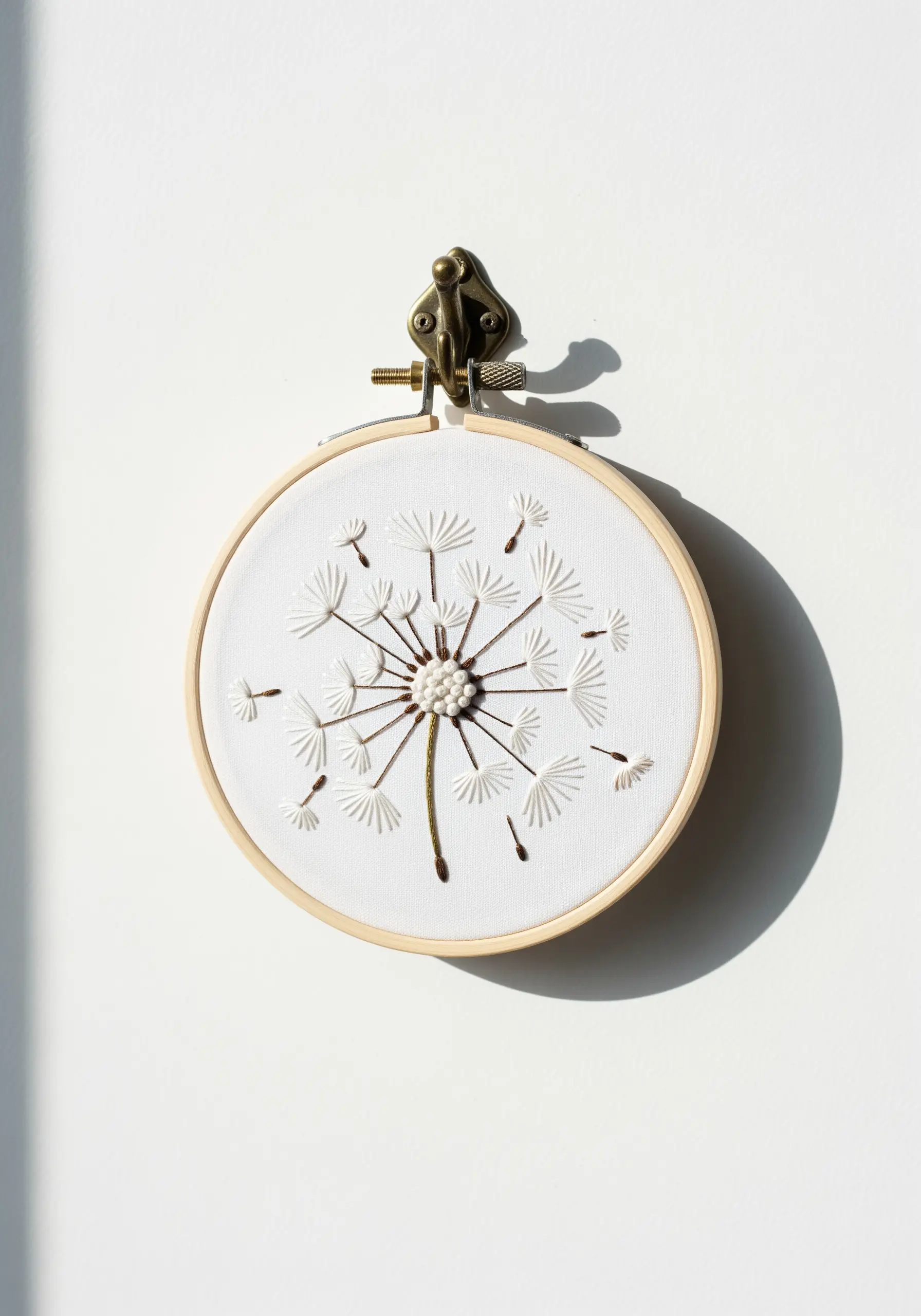 A delicate white-on-white embroidered dandelion with French knot center and straight stitch seeds.