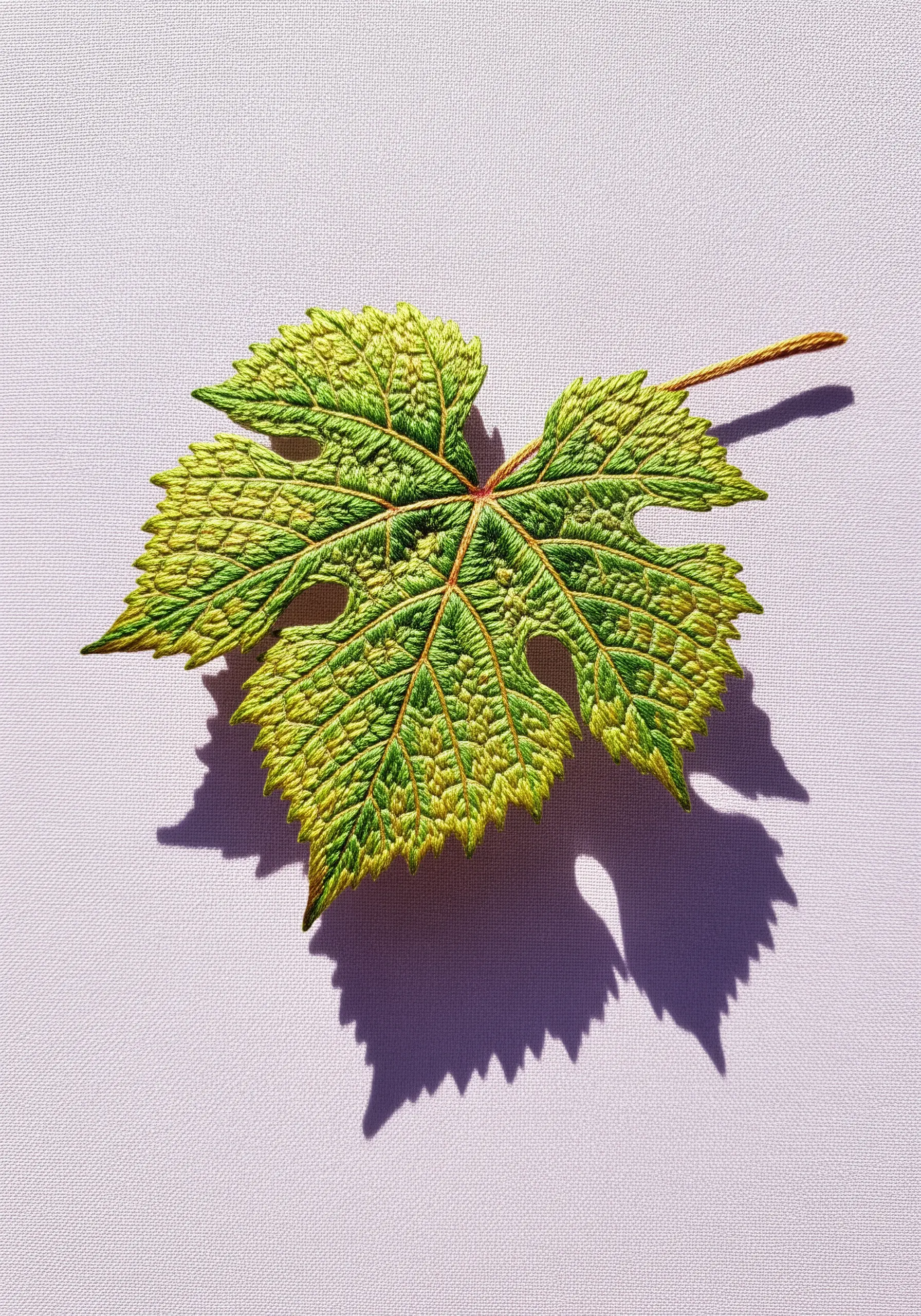 A highly textured embroidered grape leaf with dense stitching creating internal shadows.