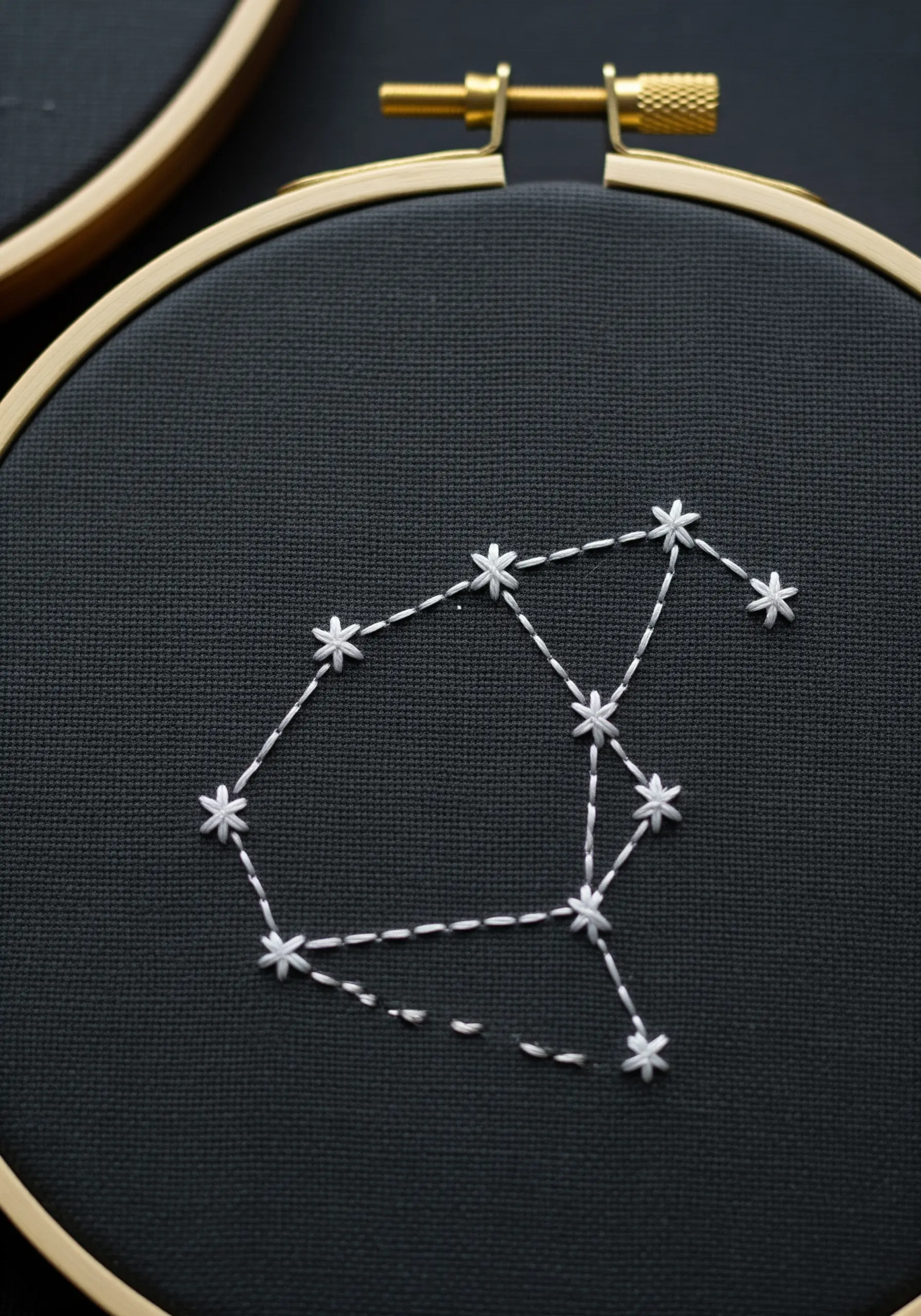 Embroidered constellation on black fabric using star stitches and dashed lines.