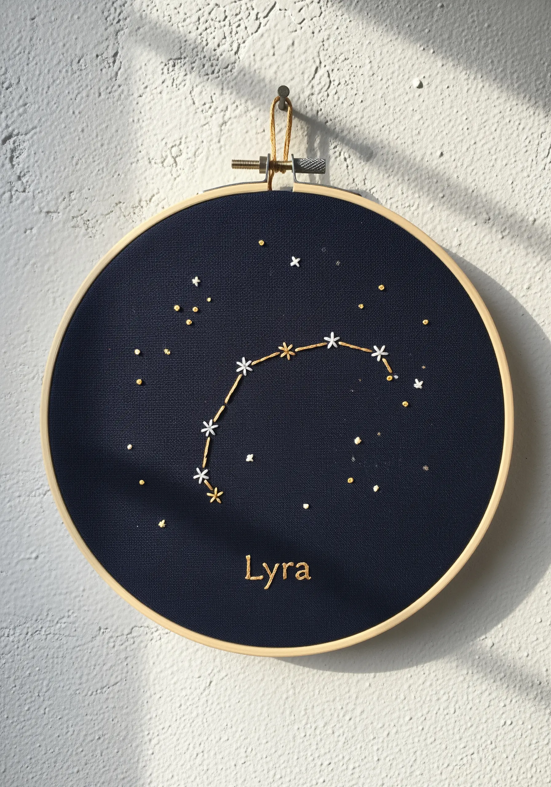 Lyra constellation embroidered with white and gold thread on navy fabric.