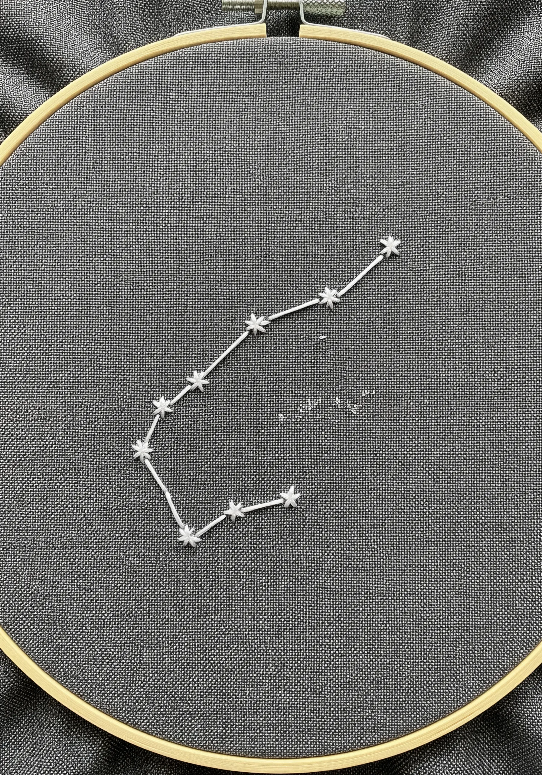 A constellation embroidered with white star stitches and connecting lines on gray fabric.