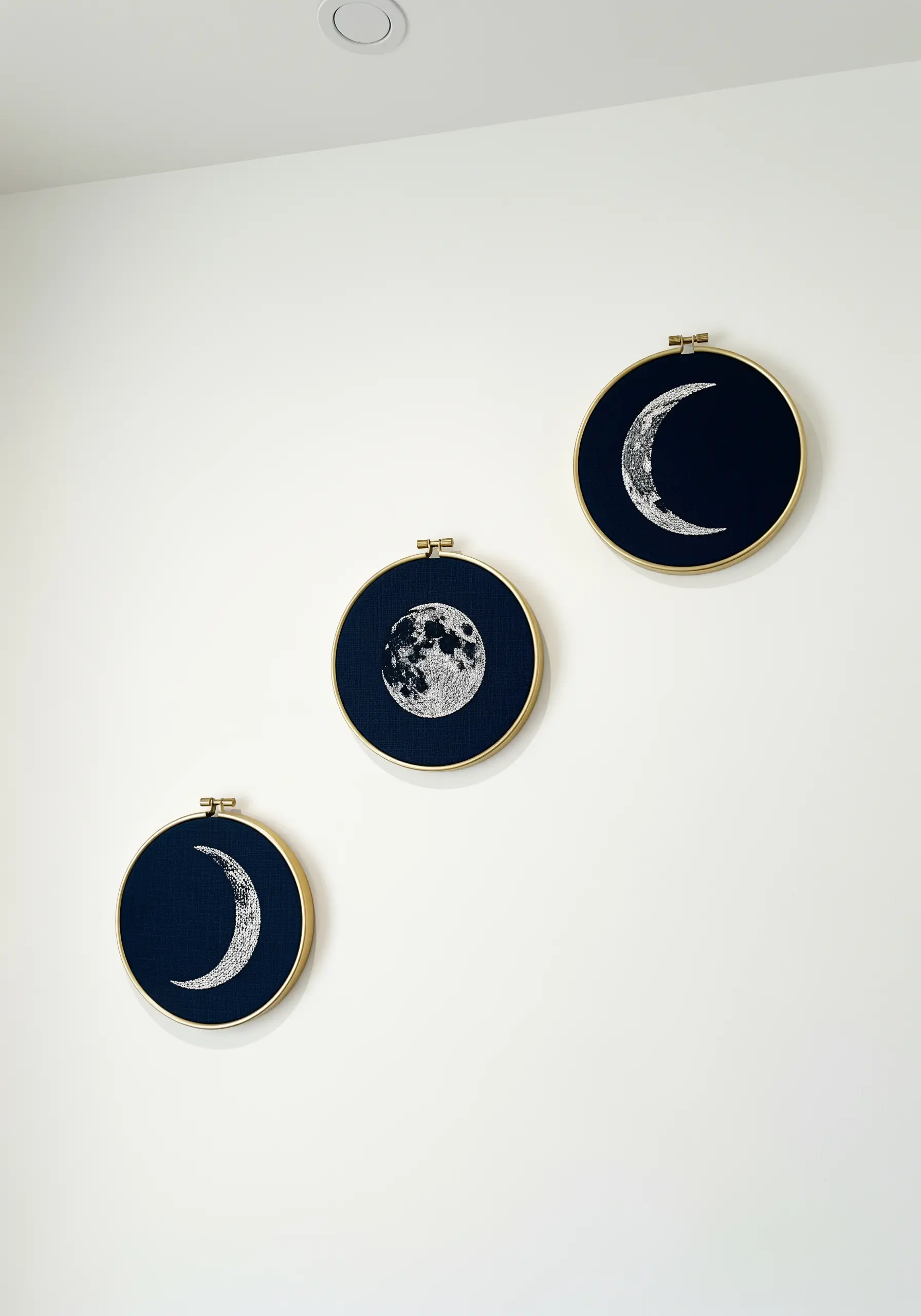 Three embroidery hoops on navy fabric depicting phases of the moon in white thread.