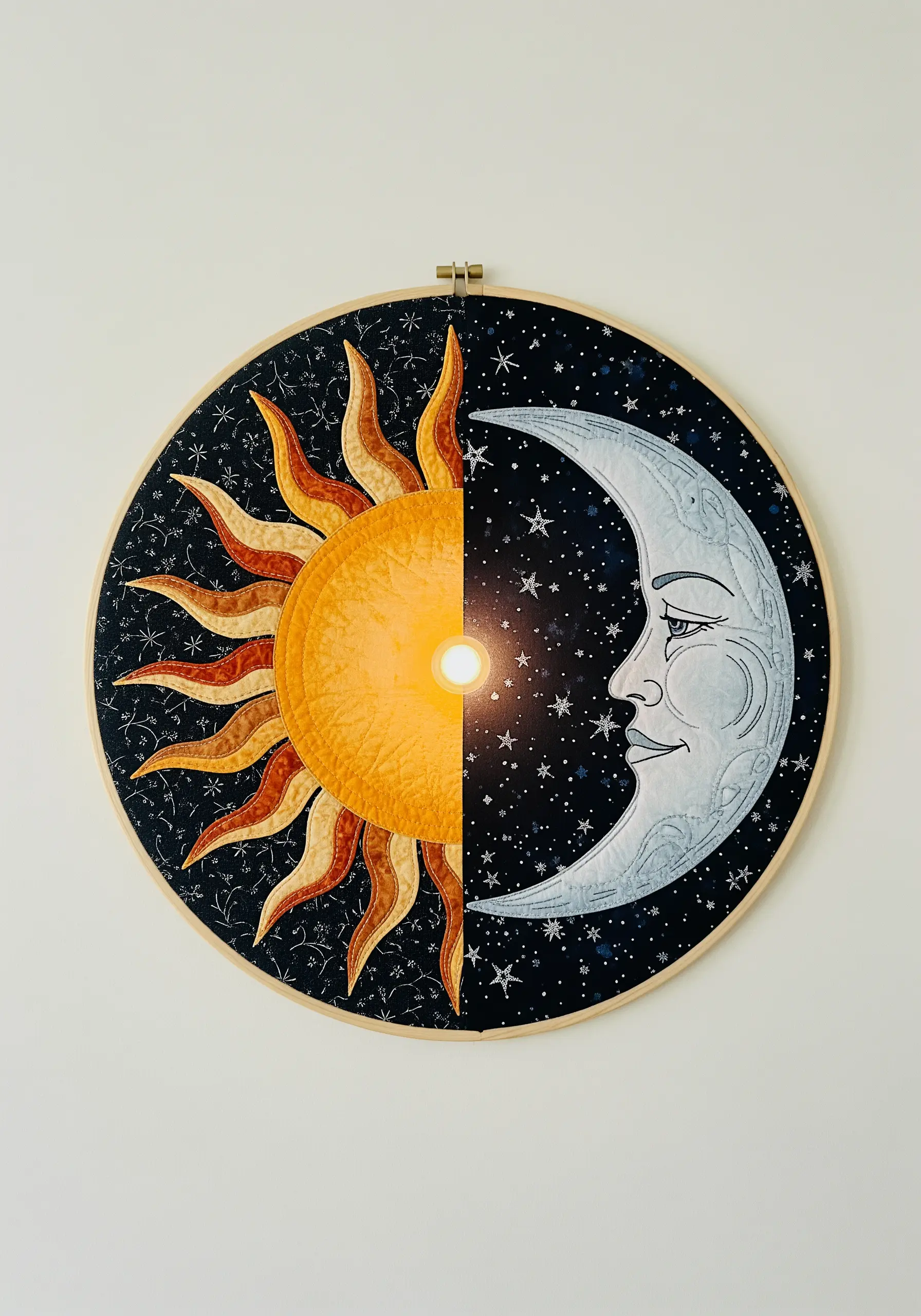 Appliqué art in a hoop showing a sun on one side and a moon on the other.