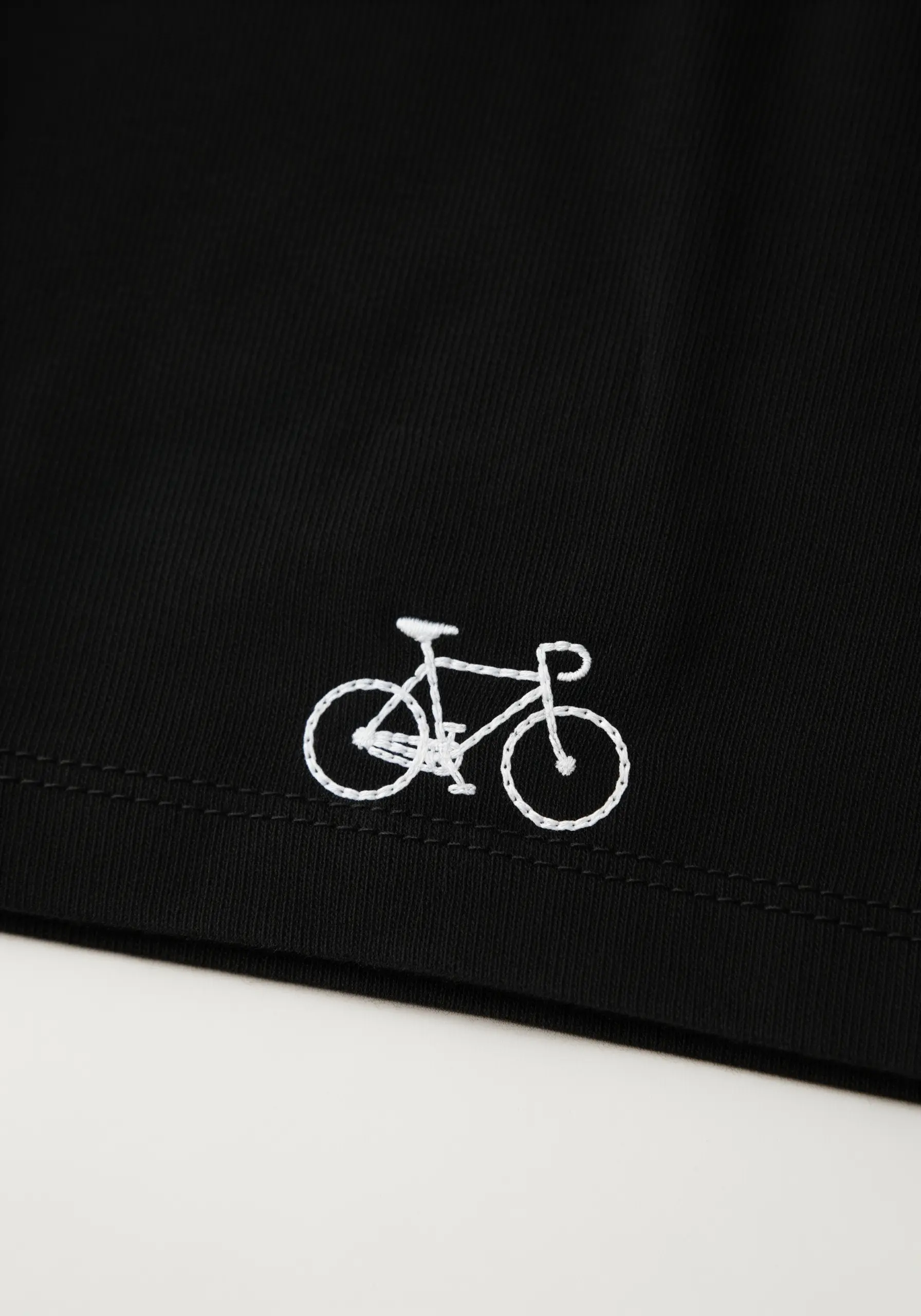 A tiny white outline of a bicycle embroidered on the hem of a black garment.