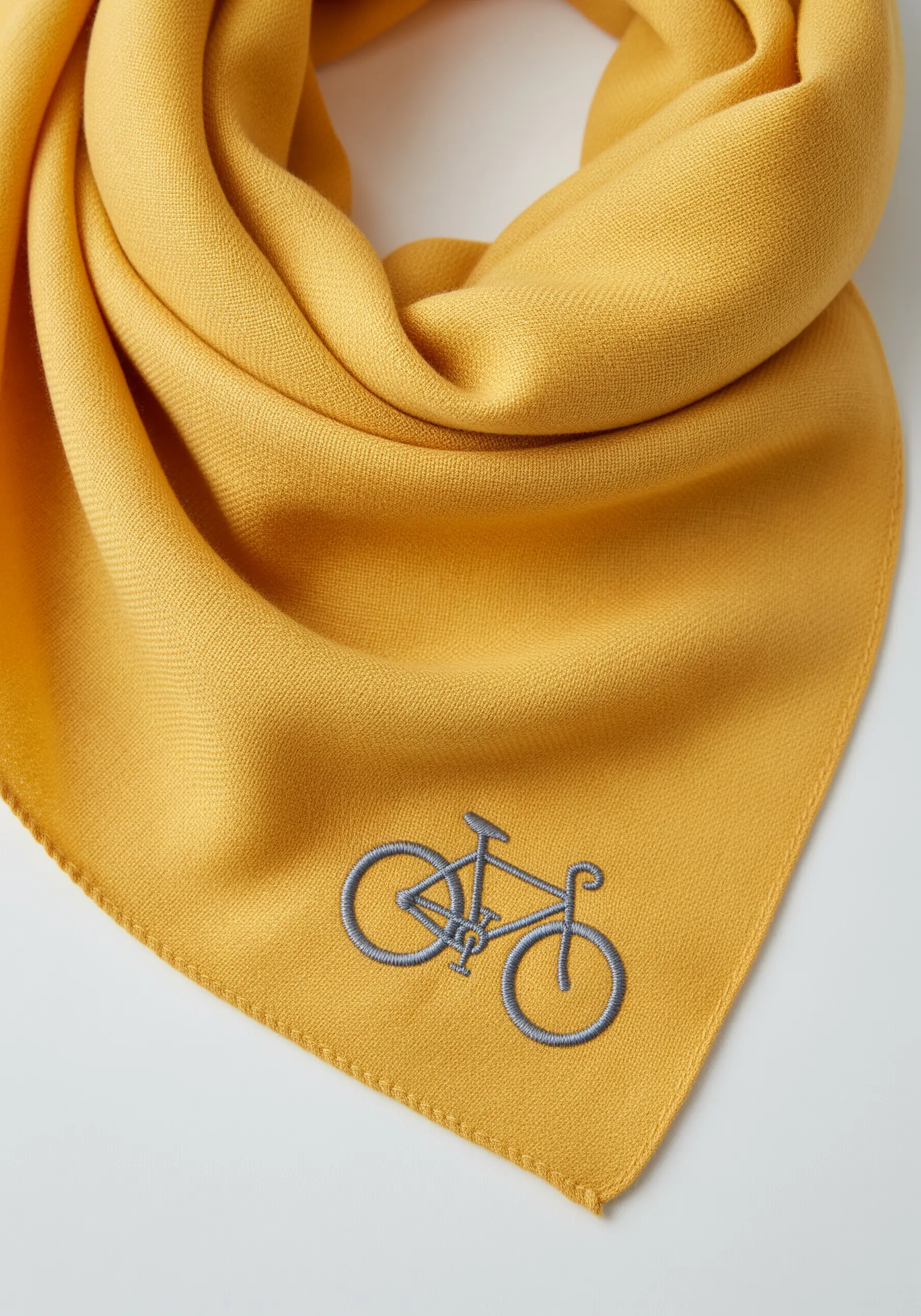 An embroidered outline of a classic bicycle in grey thread on a yellow scarf.