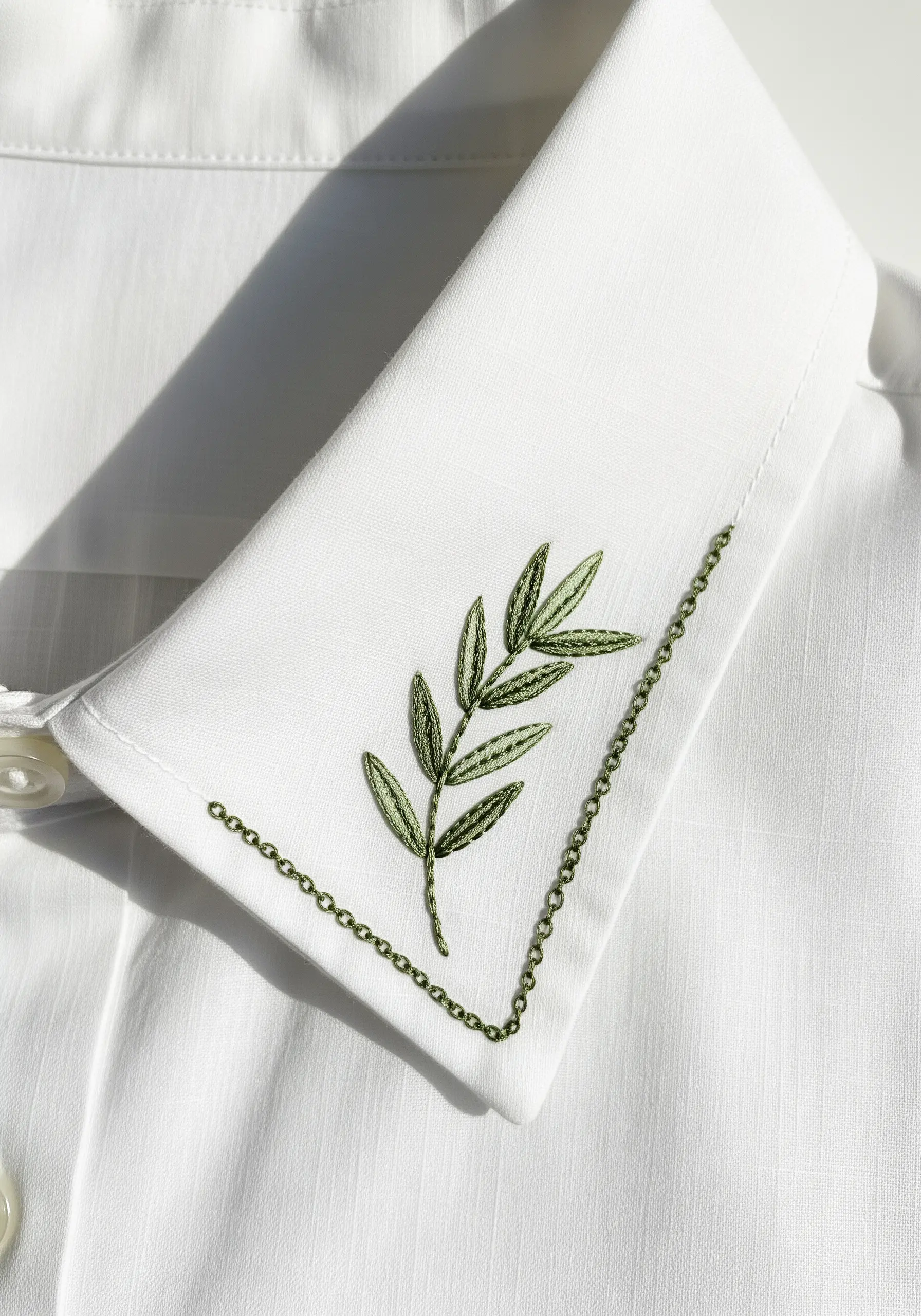 Olive branch embroidered on a white shirt collar with a delicate chain stitch border.