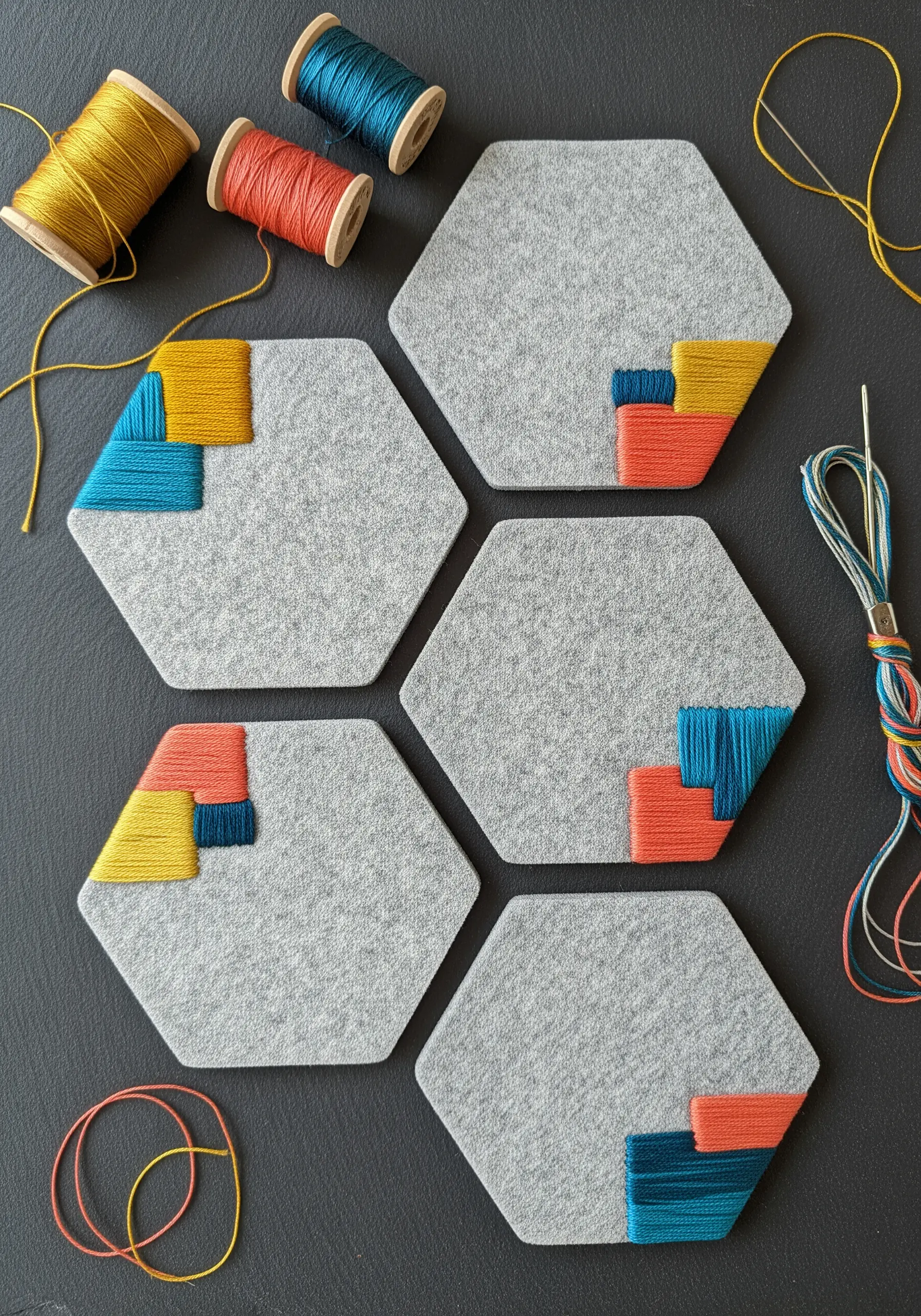 Geometric color-blocking with satin stitch on hexagonal grey felt coasters.