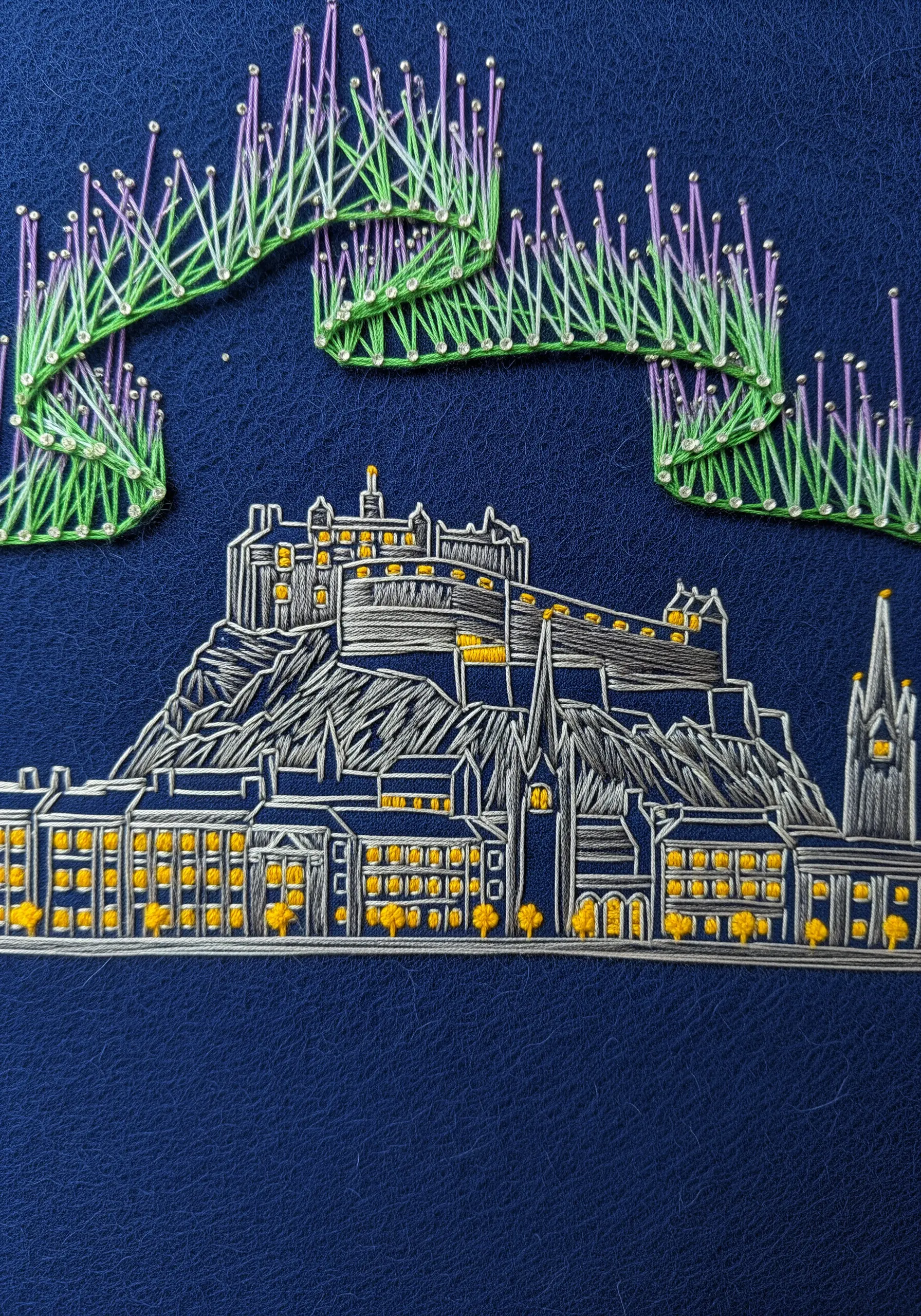 Embroidery of Edinburgh Castle with the Northern Lights stitched in flowing green thread above it.