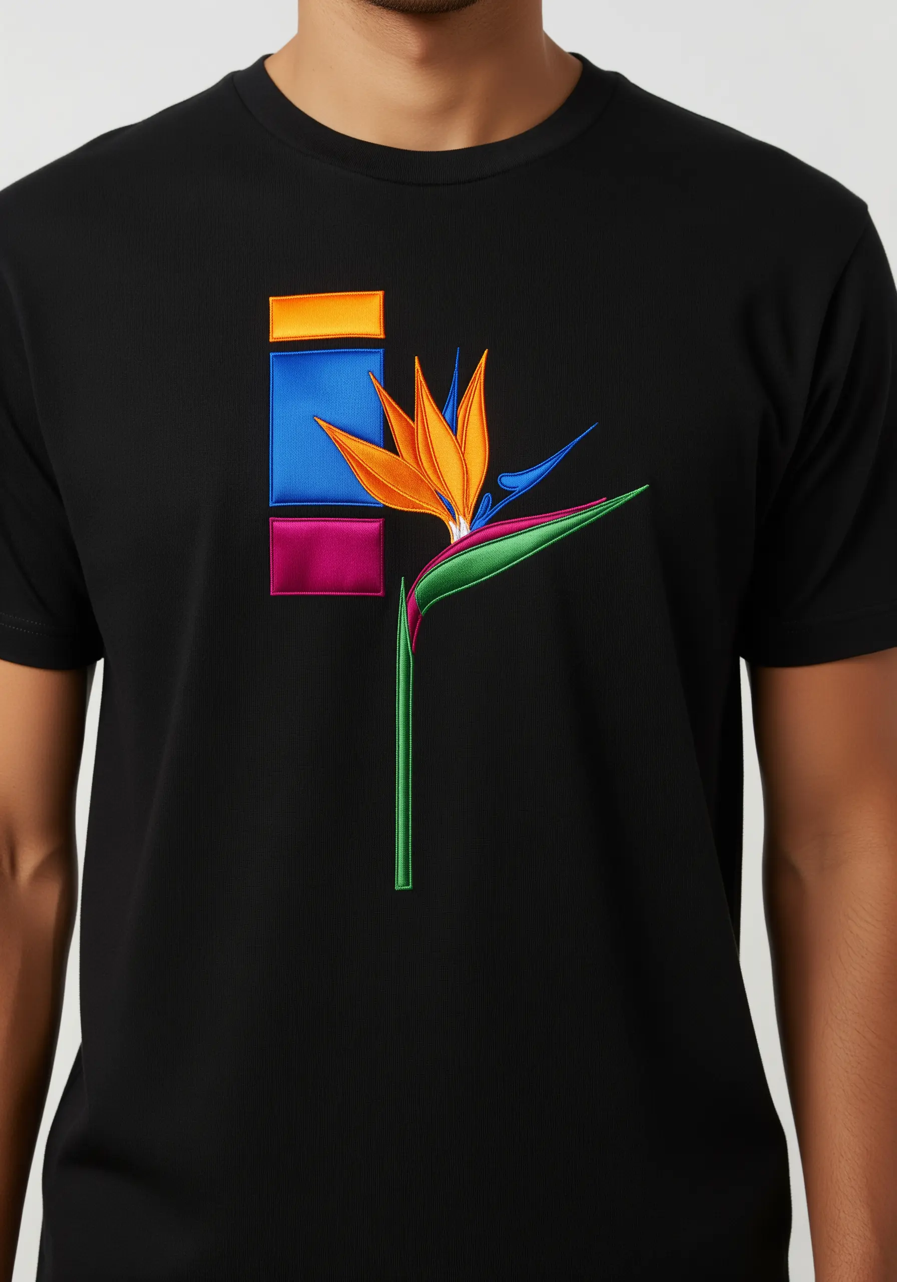 A bird of paradise flower embroidered over geometric color blocks on a black t-shirt.