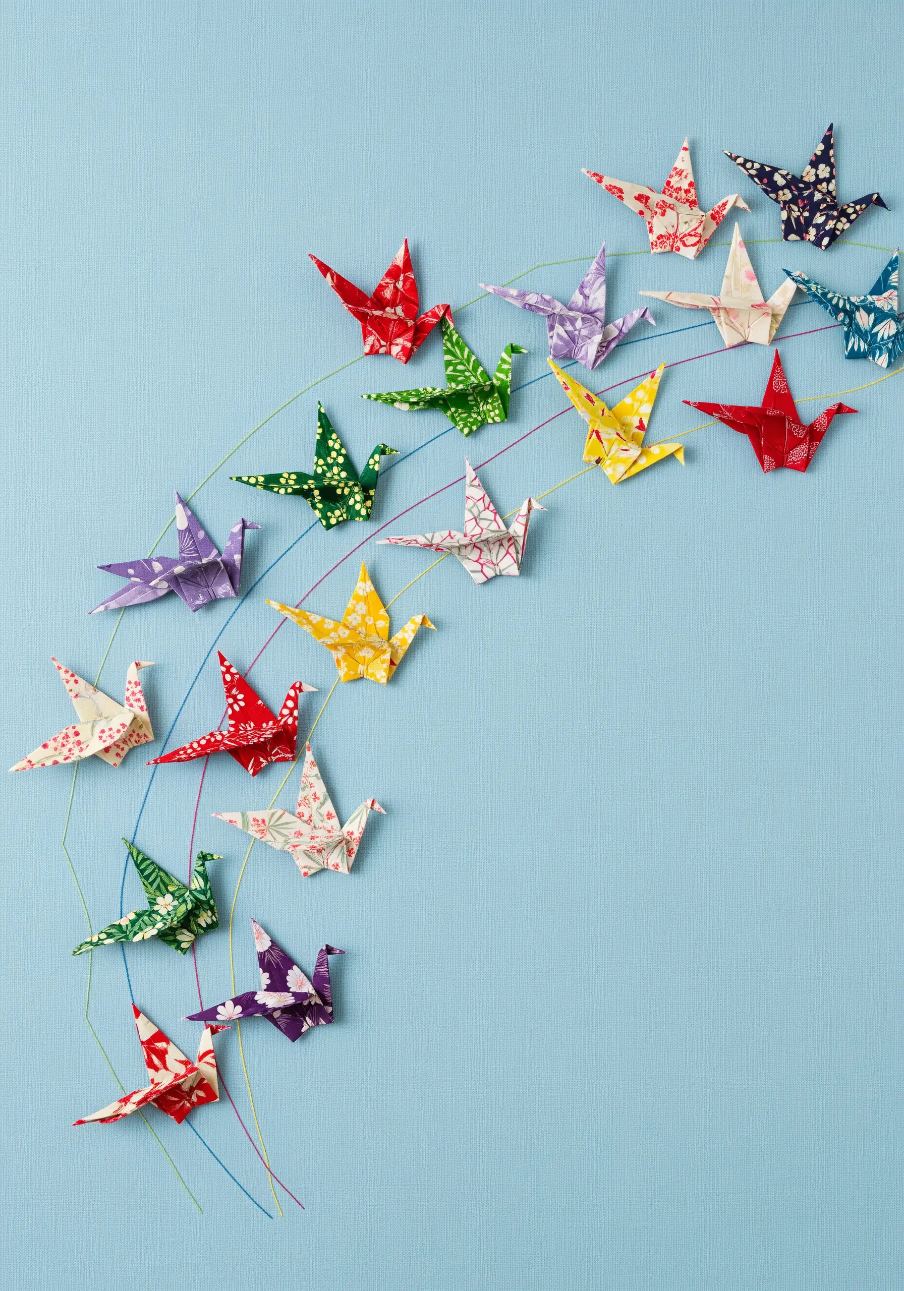 A collection of colorful origami paper cranes attached to fabric with delicate stitched flight paths.