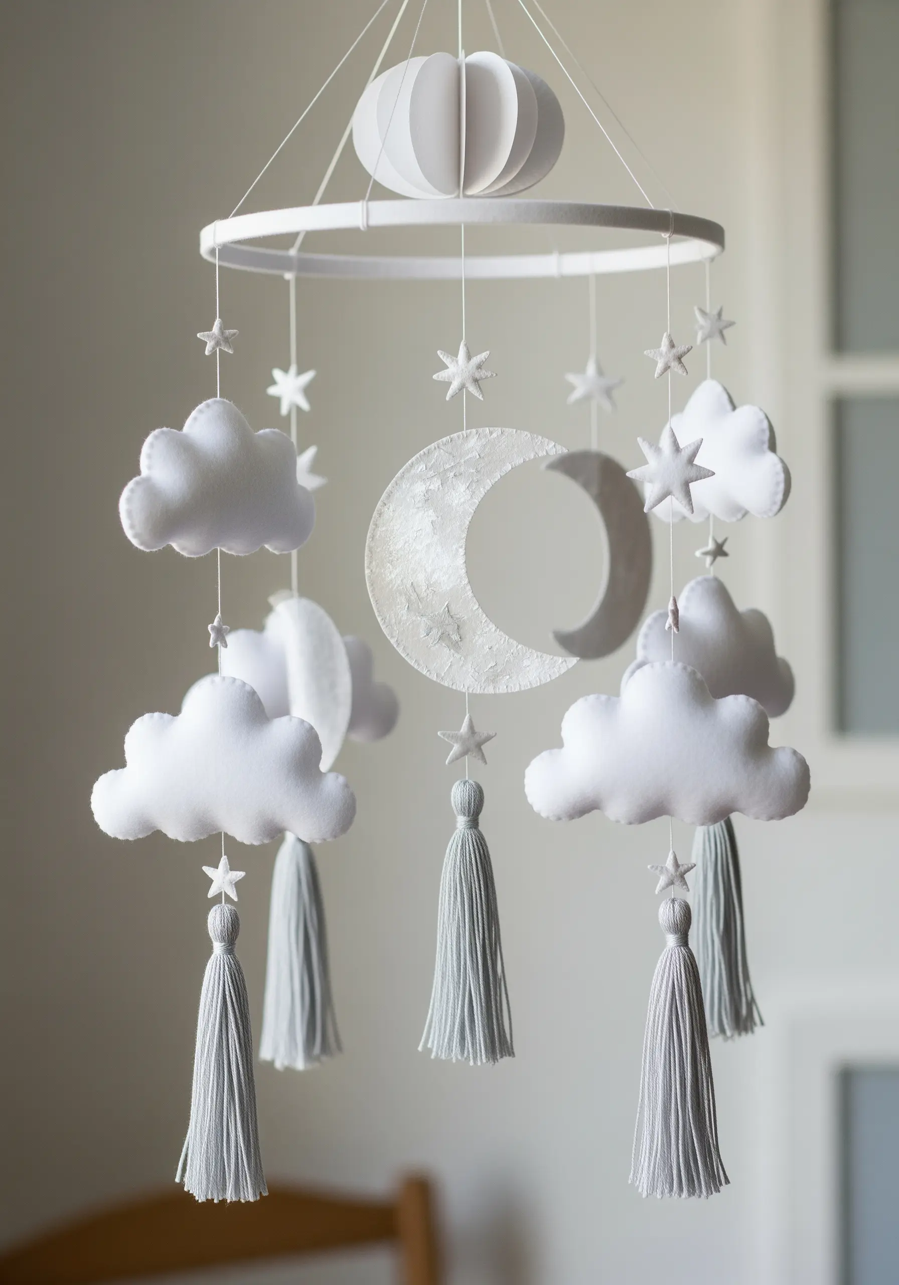 A nursery mobile with stitched felt clouds and a central, multi-layered paper moon.