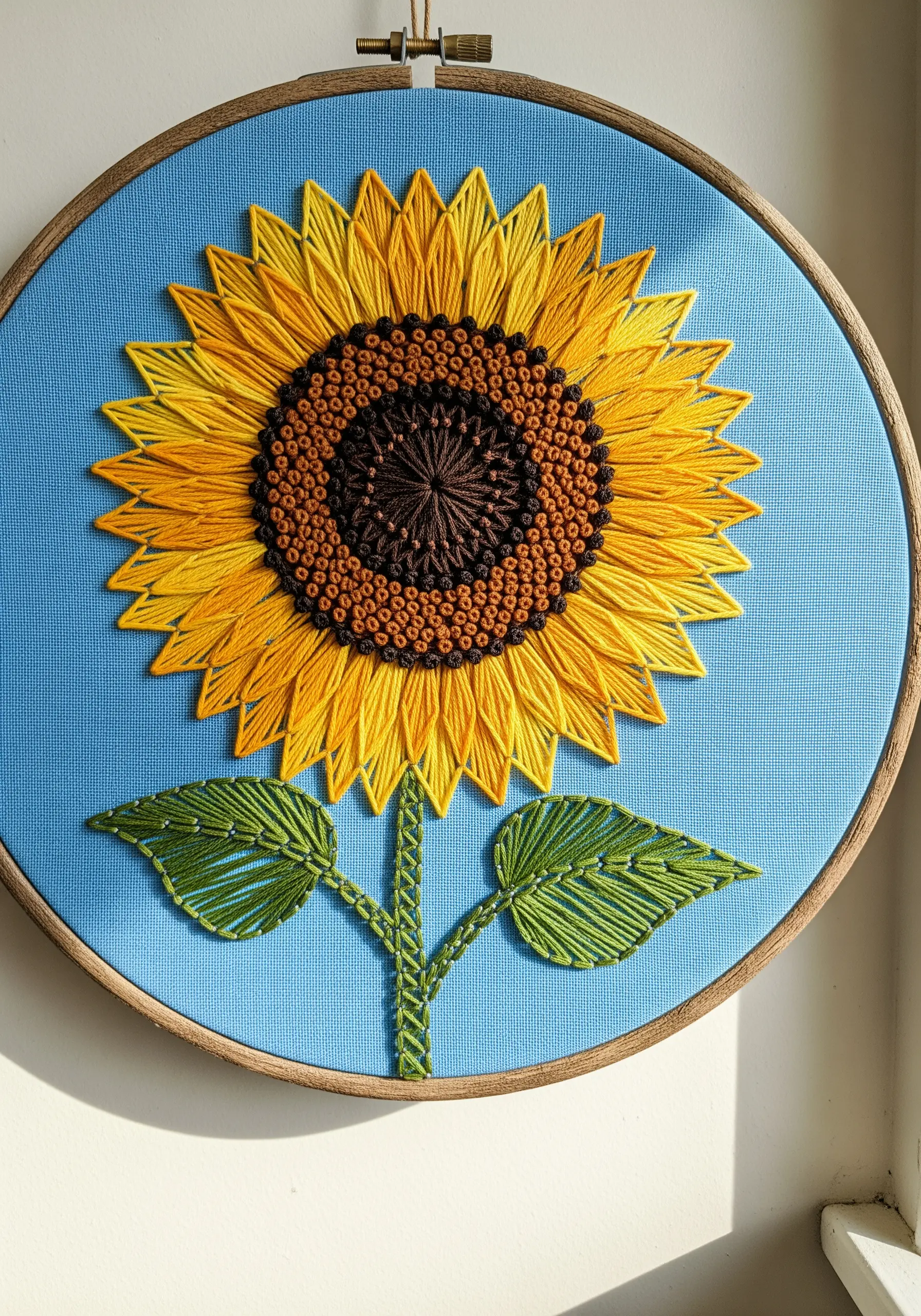 Embroidered sunflower with long-stitch petals and a French knot center.