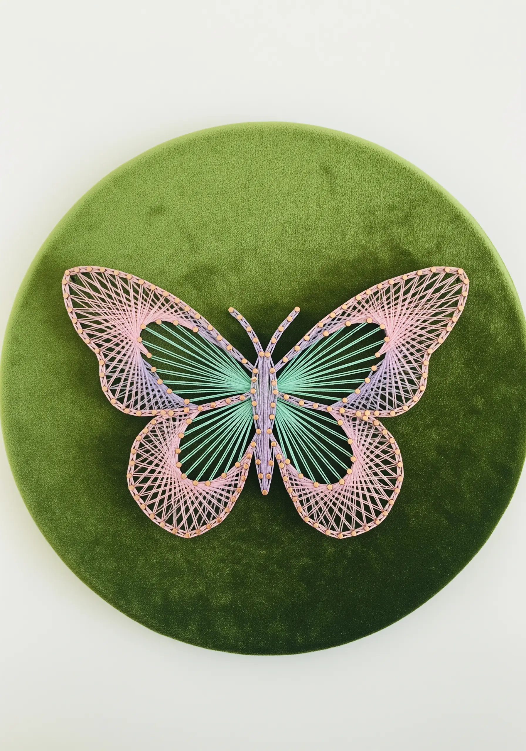Delicate string art butterfly in pink, mint, and purple on a round olive velvet canvas