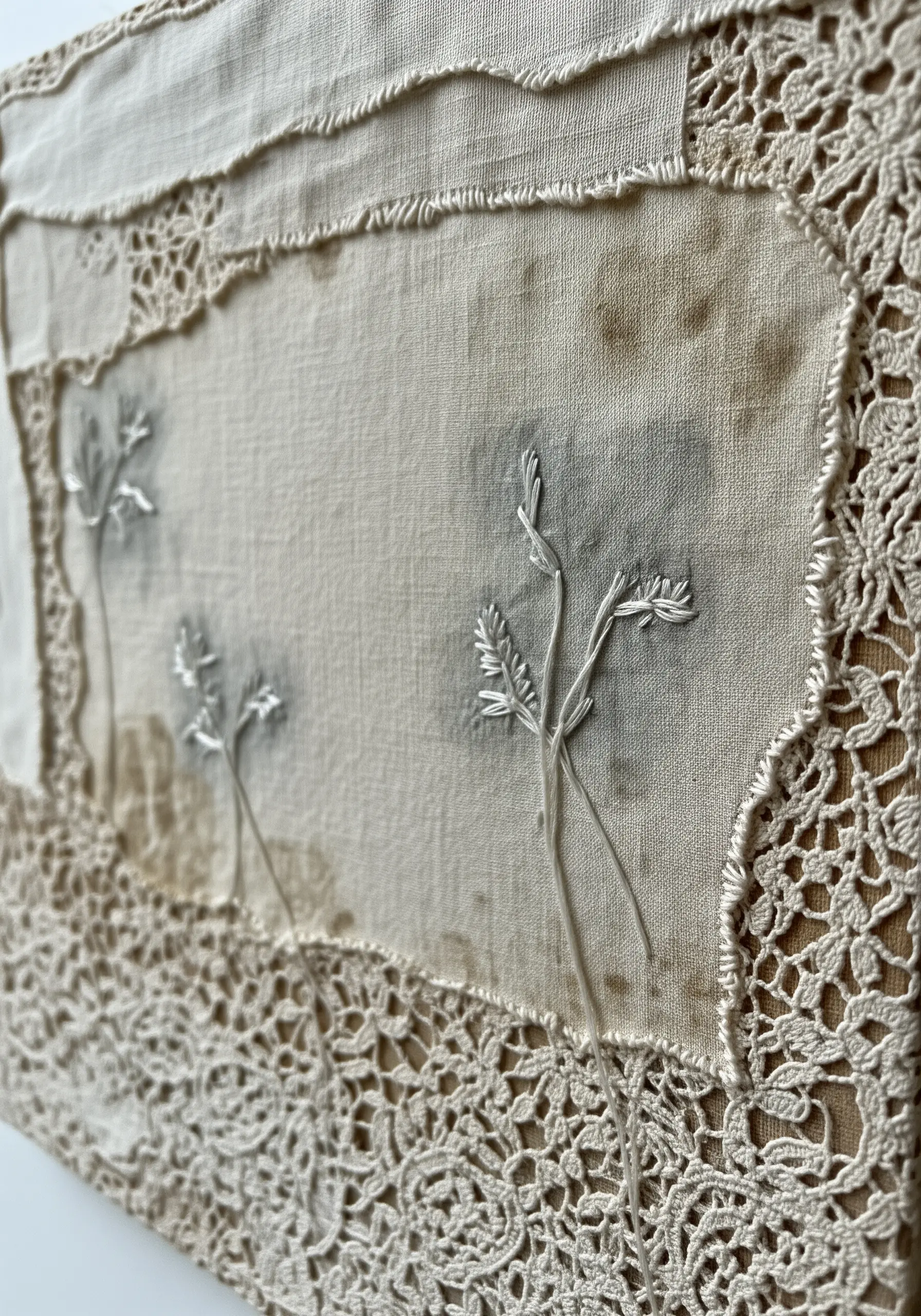 Vintage collage of stained linen and lace with delicate white botanical embroidery.