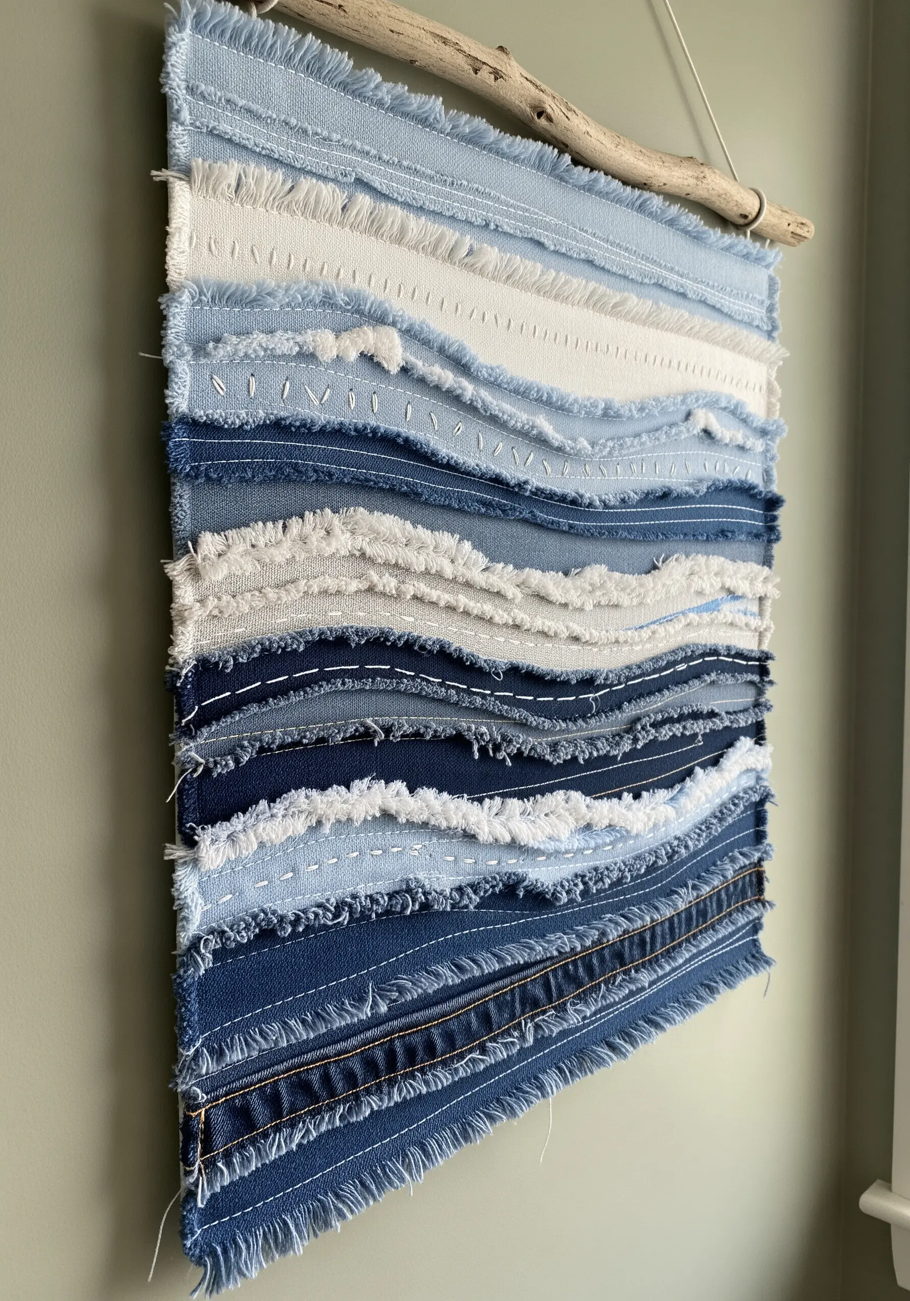 Wall hanging made from layered strips of raw-edge denim in shades of blue and white.