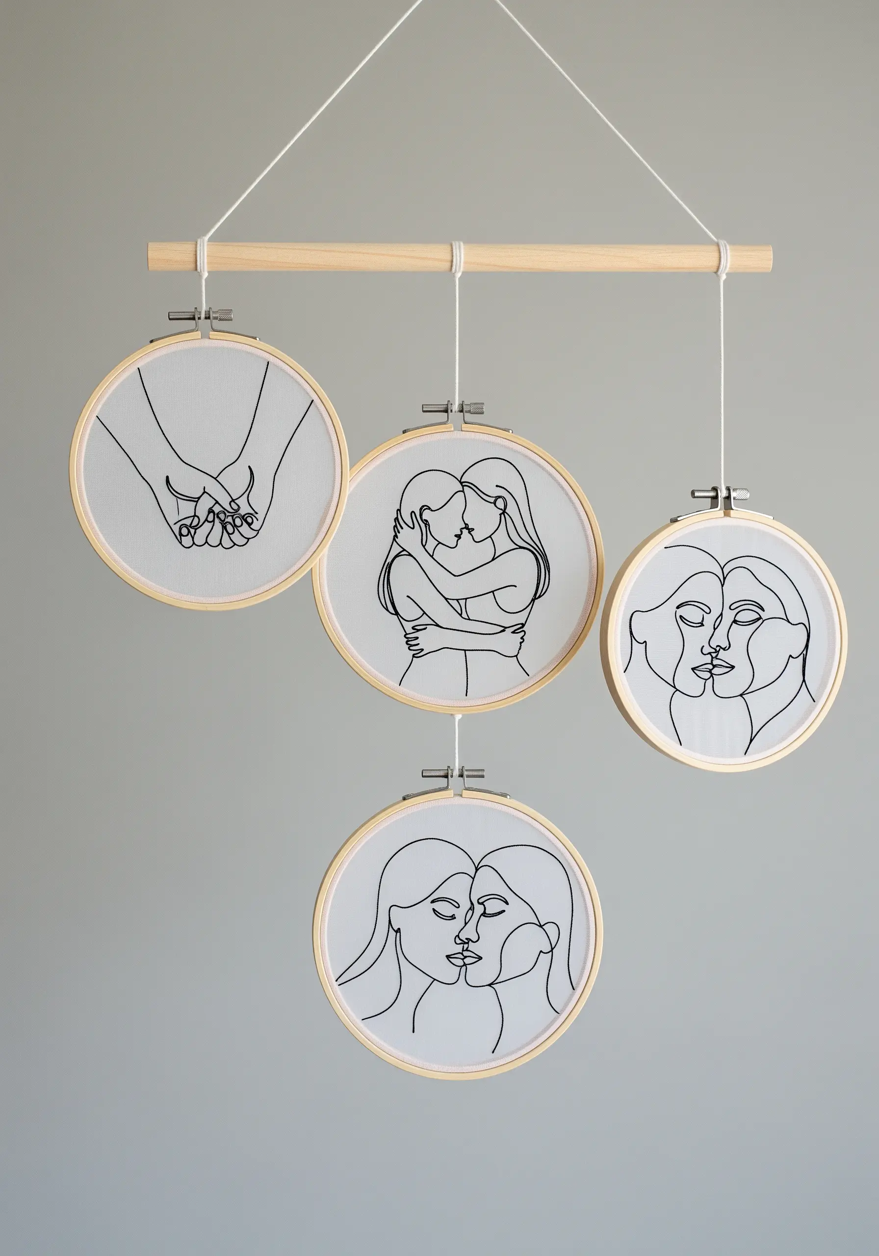 A nursery mobile made from four embroidery hoops with line art, hanging from a wooden dowel.