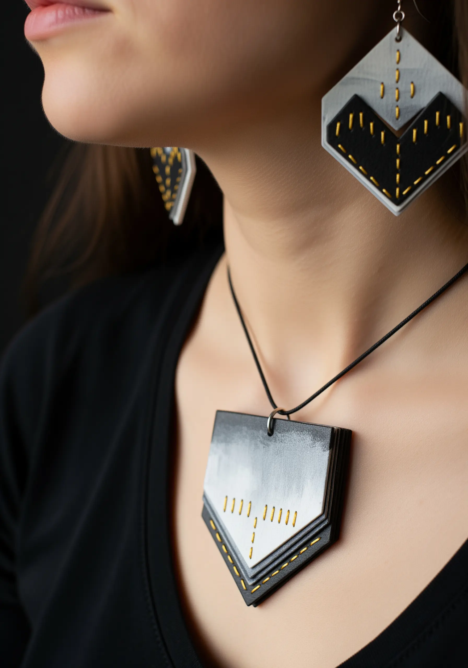 A woman wearing a geometric necklace and earrings made from painted wood with stitched details.