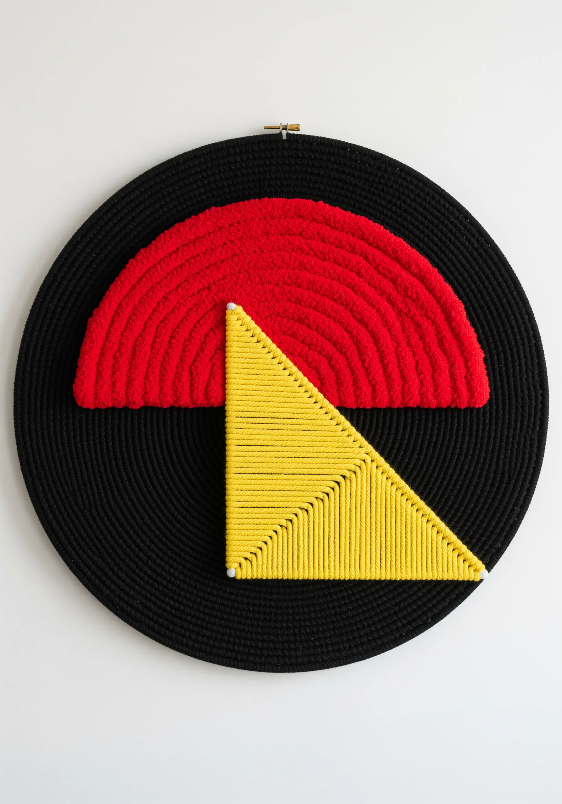 Abstract geometric yarn art in a black hoop with a plush red semi-circle and a wrapped yellow triangle.