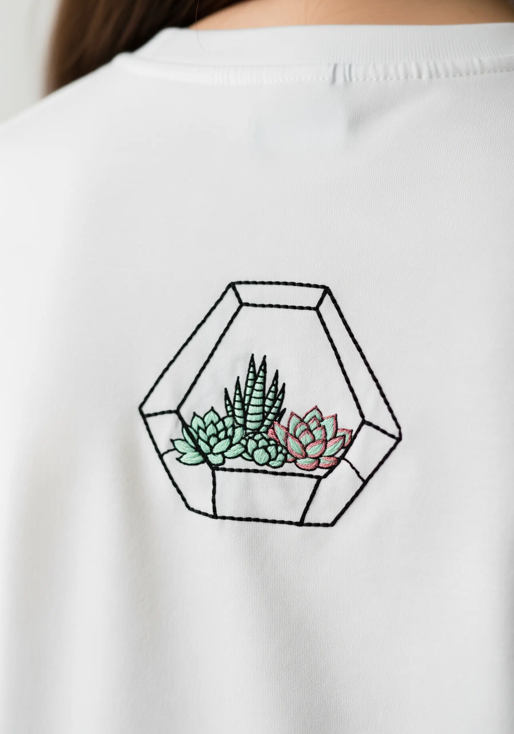 A geometric glass terrarium with small succulents embroidered on the back of a shirt.