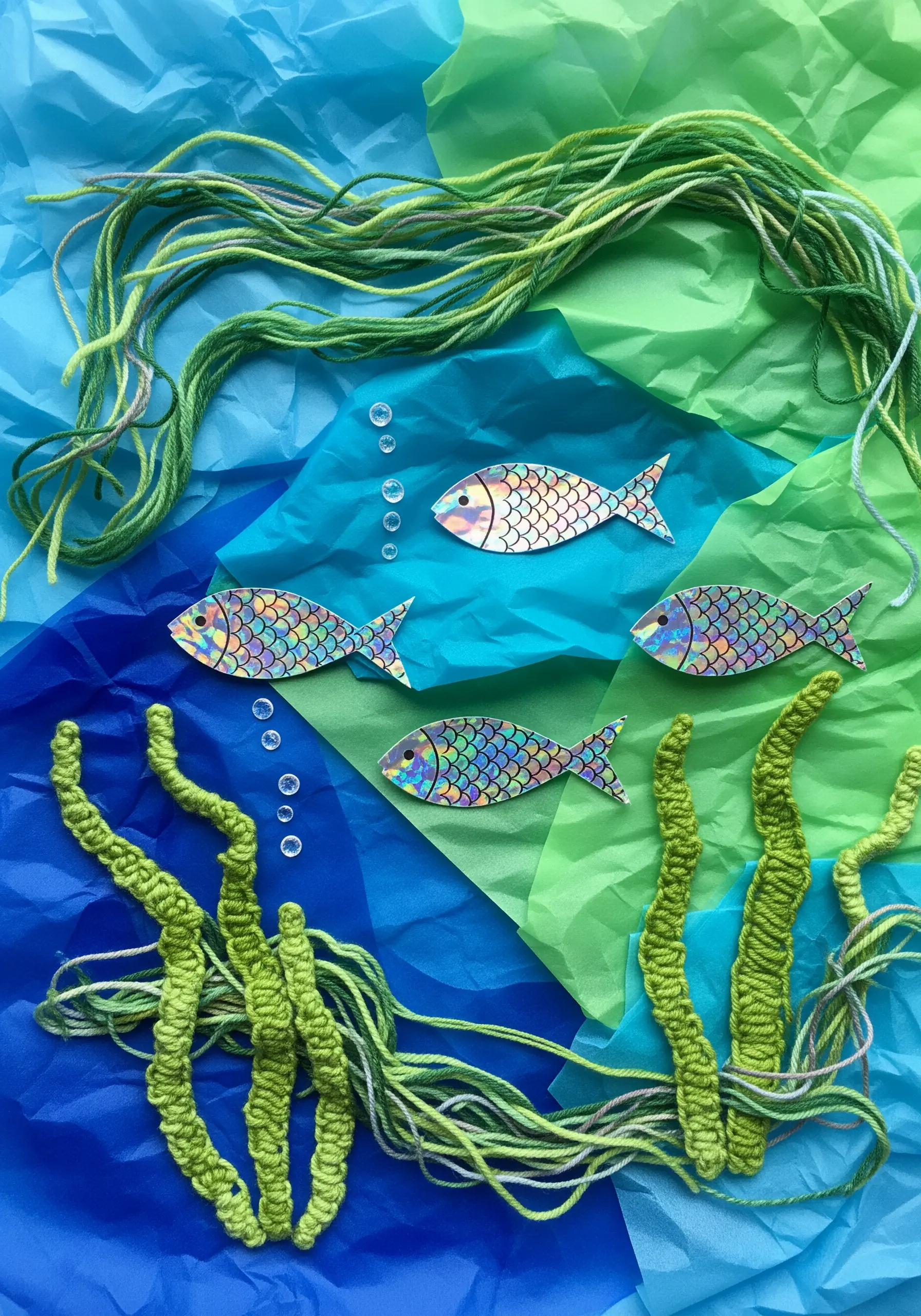 An underwater scene made with tissue paper and chunky green yarn couched down to form seaweed.
