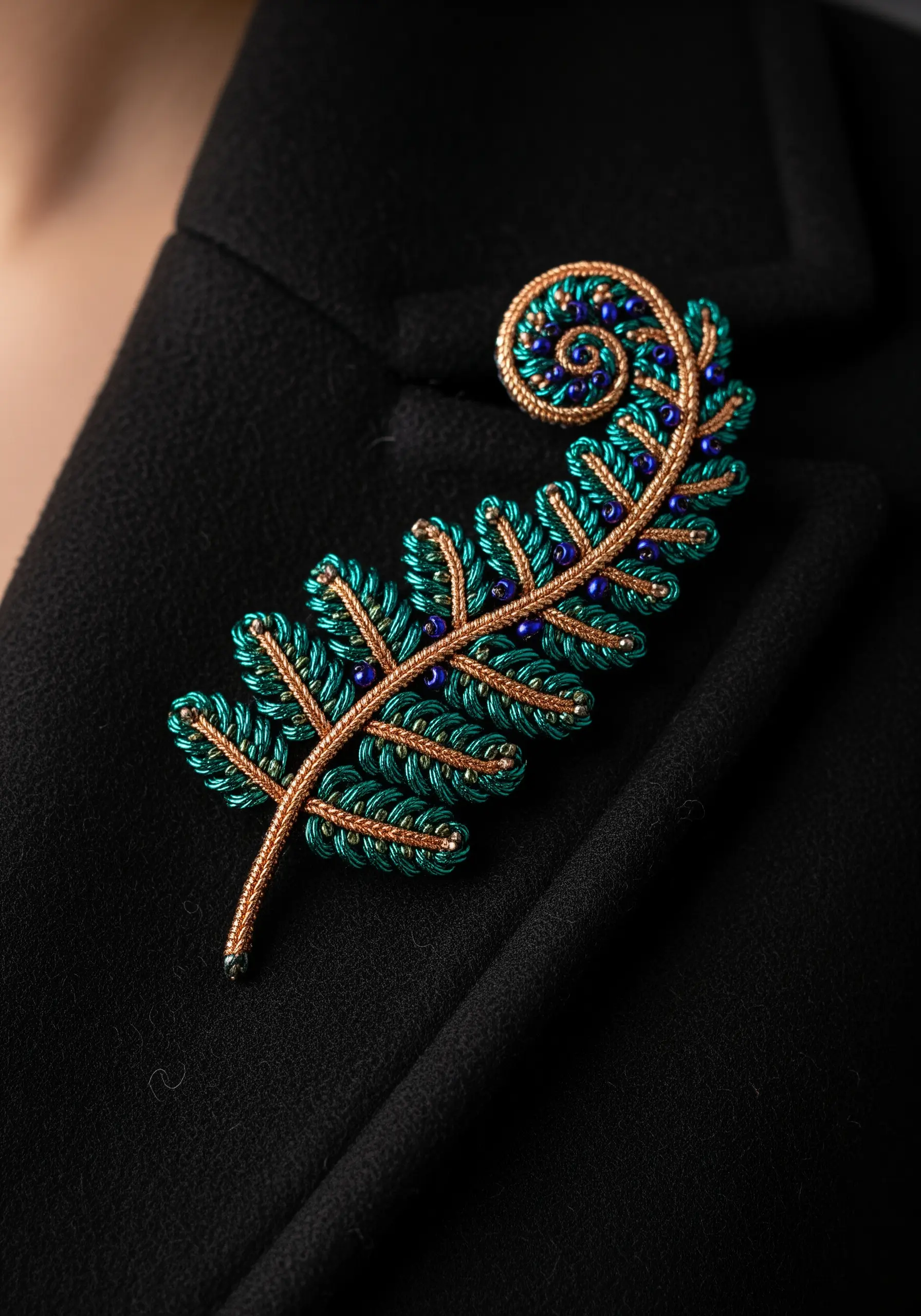 An intricate, dimensional fern brooch made with wrapped wire, emerald thread, and tiny blue beads.