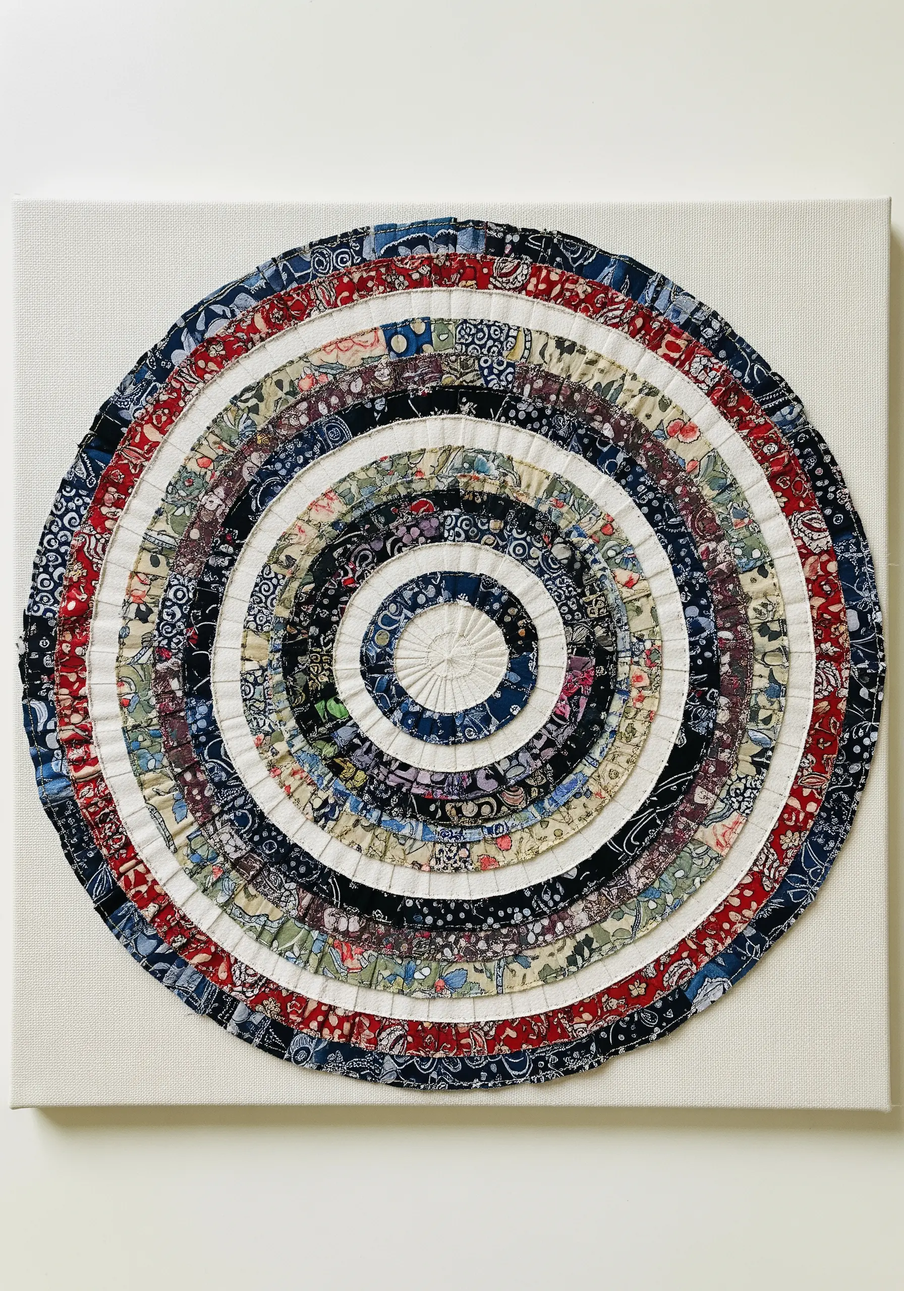 A circular medallion on a white canvas, made from concentric rings of ruffled fabric scraps.