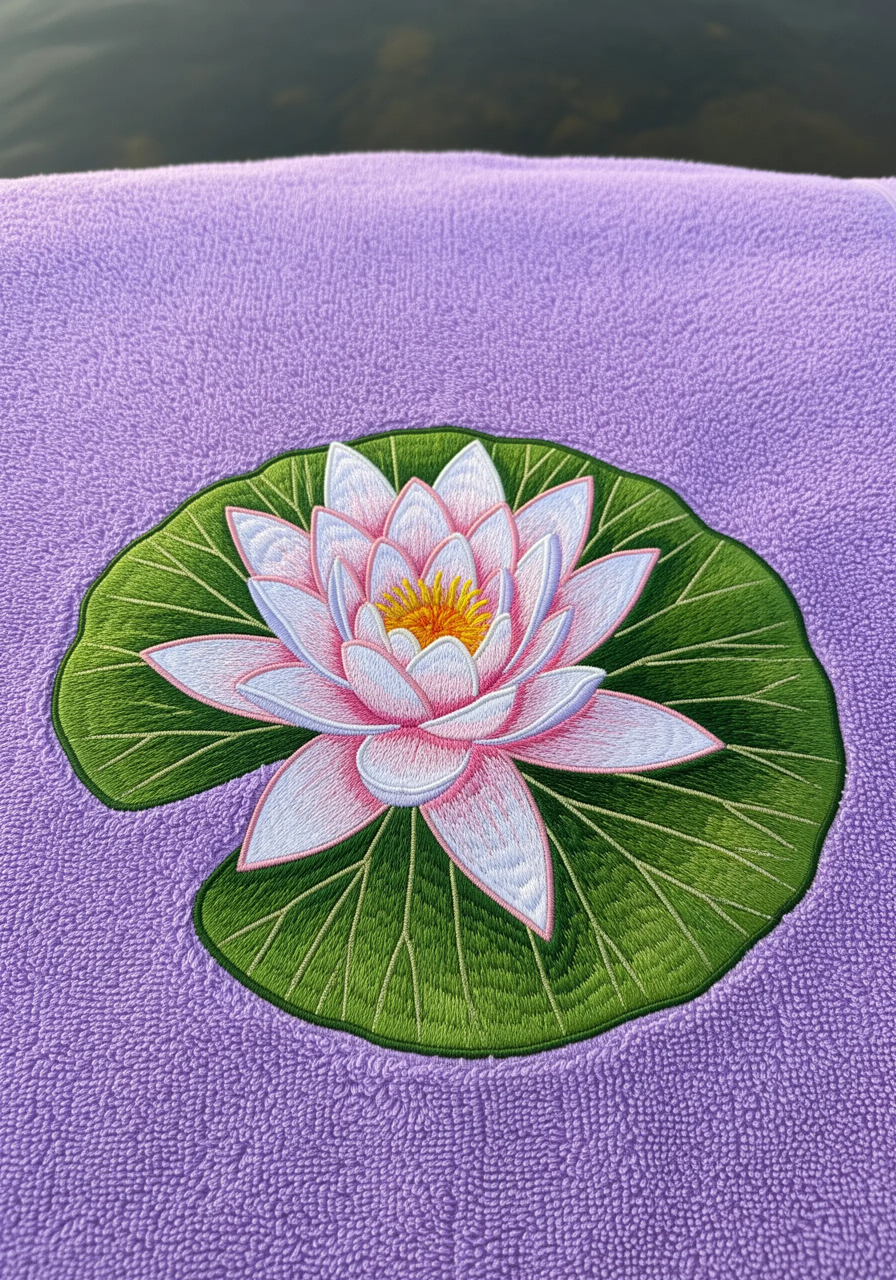 A realistic pink and white water lily on a green lily pad embroidered on a purple towel.