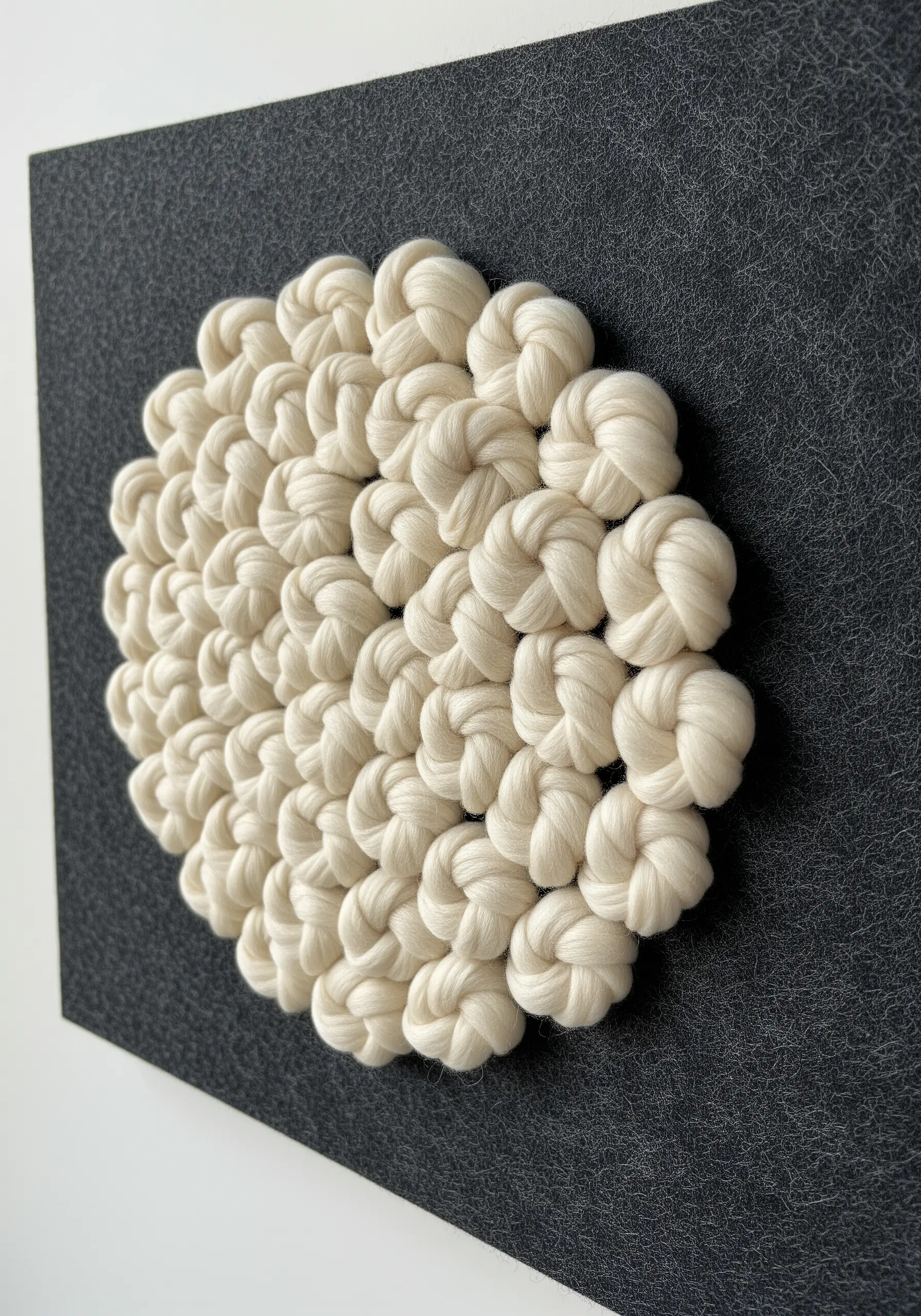 Cream-colored yarn knots creating a textured circle on a dark grey felt background.