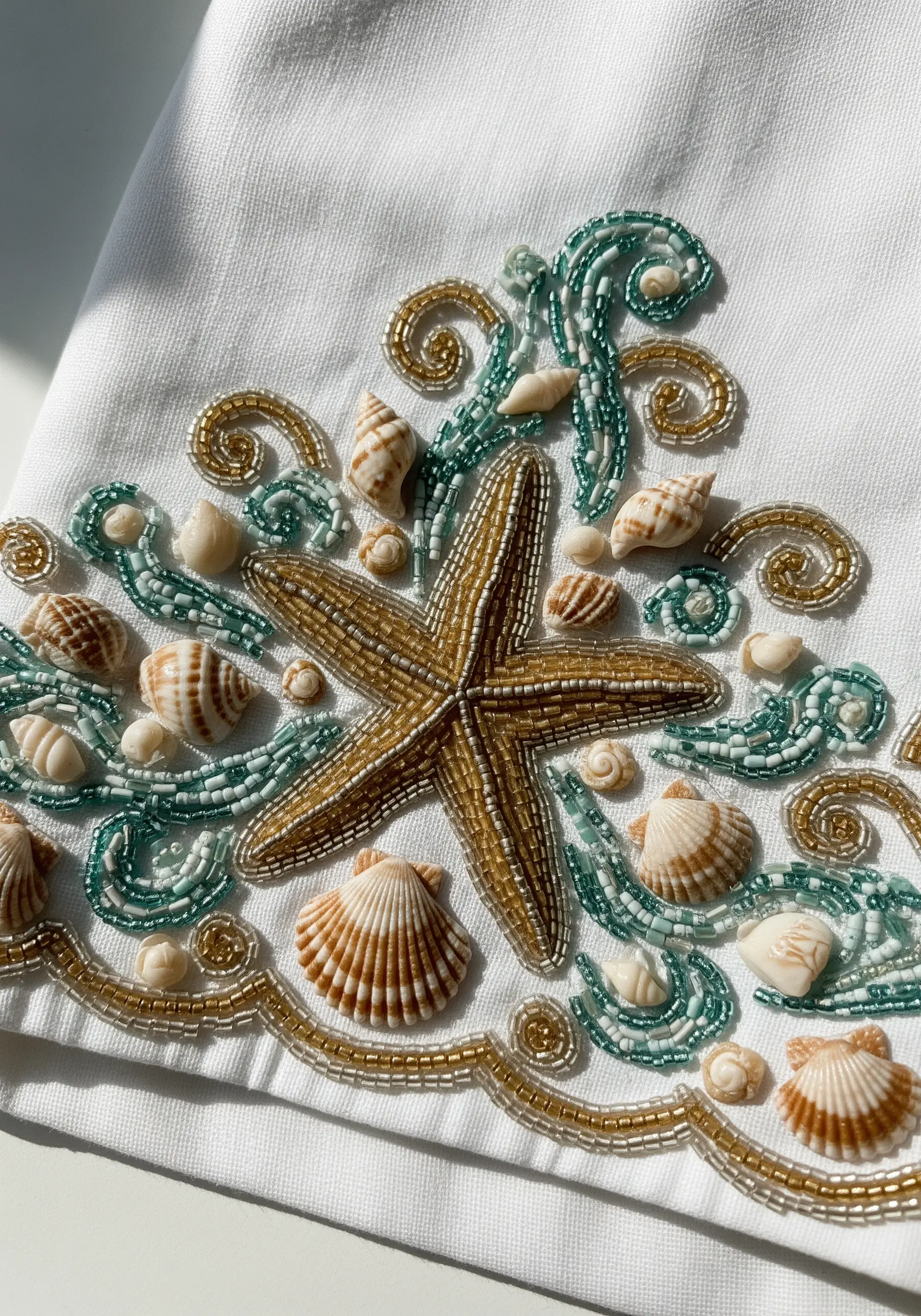 A seascape with a beaded starfish, real shells, and beaded waves on white fabric.