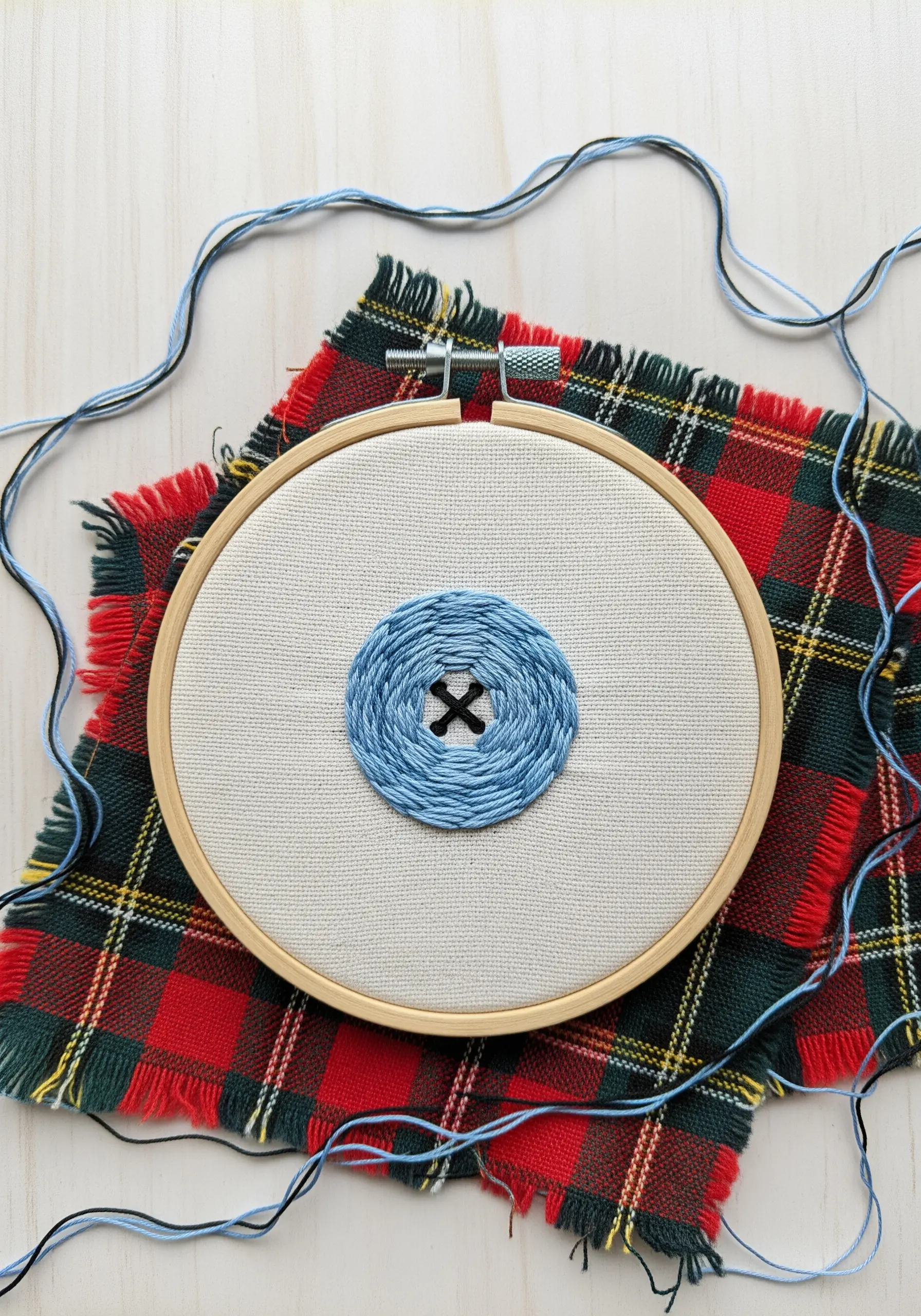 A blue button embroidered with a concentric spiral of backstitches.
