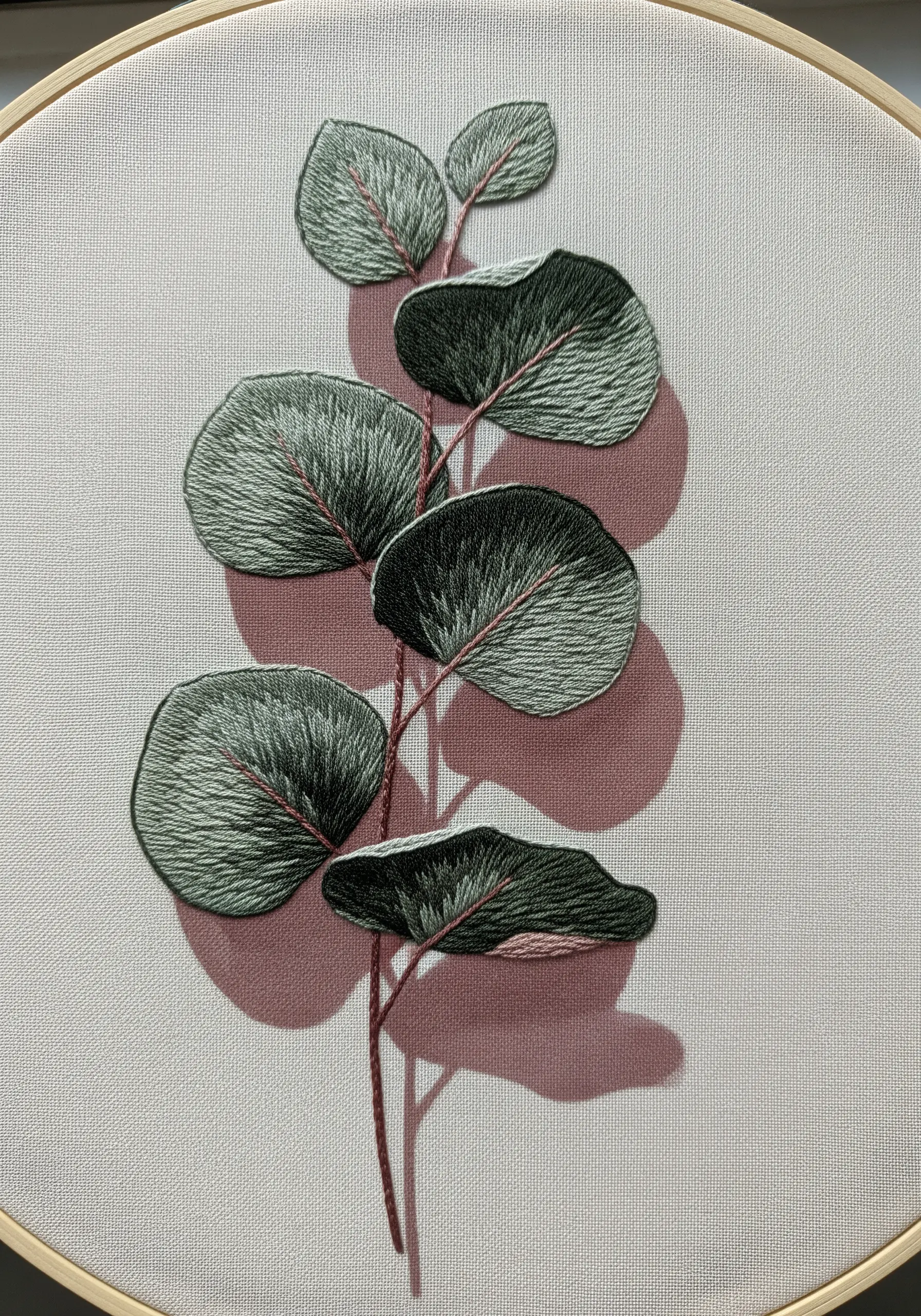 Embroidered eucalyptus leaves on light fabric with a soft, sparse shadow underneath.
