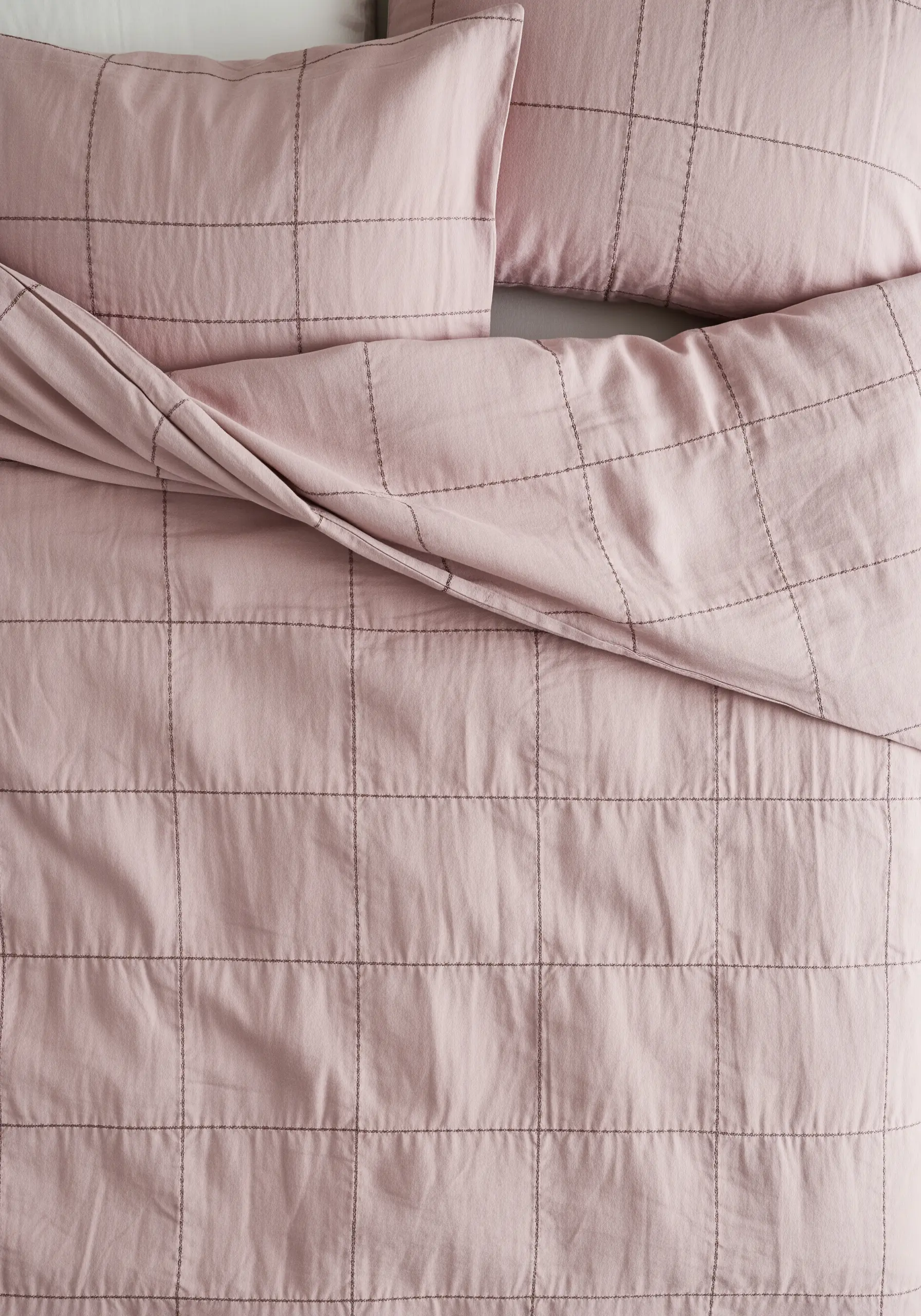 A pink duvet cover with a hand-stitched grid pattern in dark thread, creating a quilted effect.